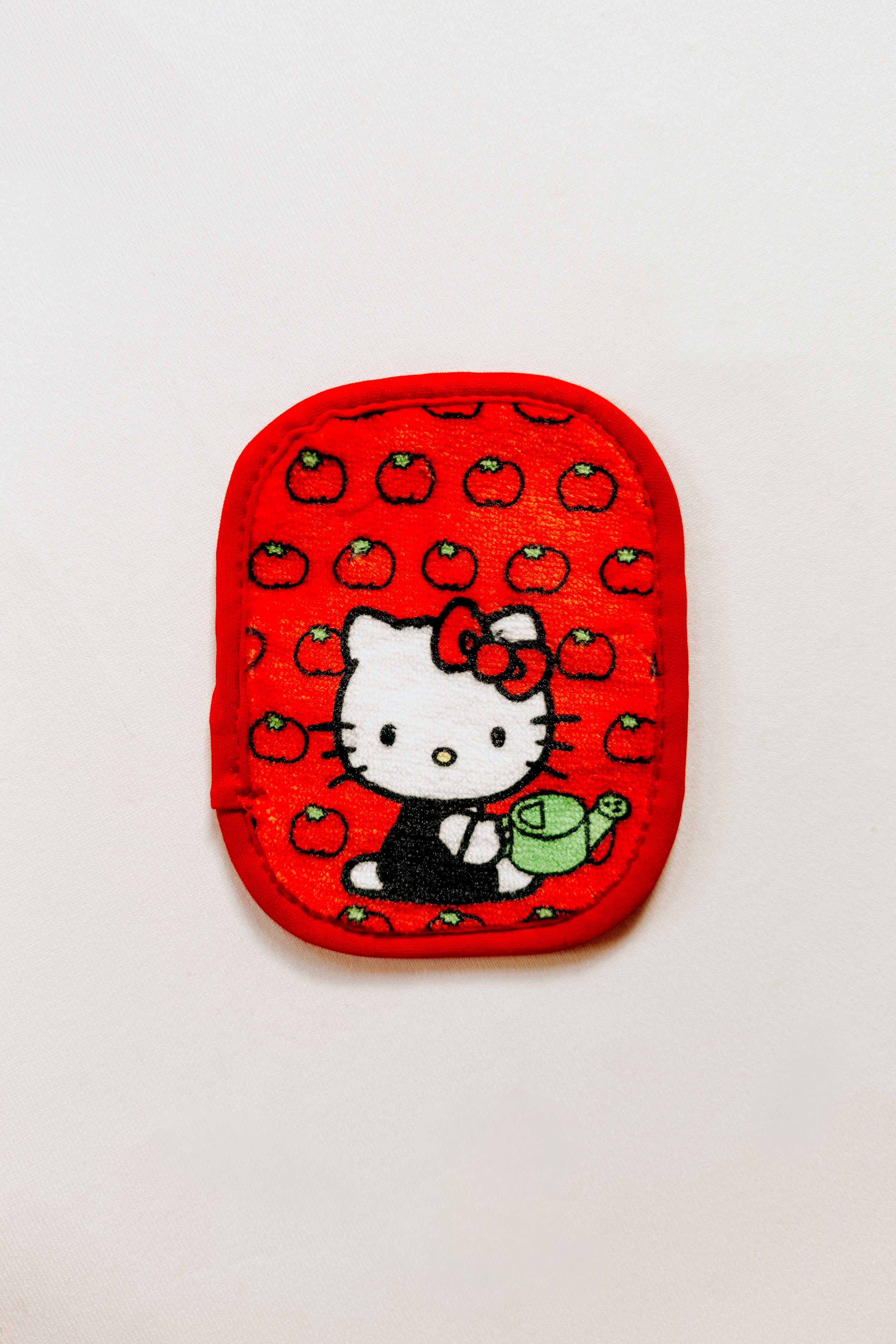 Small red reusable makeup eraser featuring Hello Kitty holding a green watering can with tomato pattern background