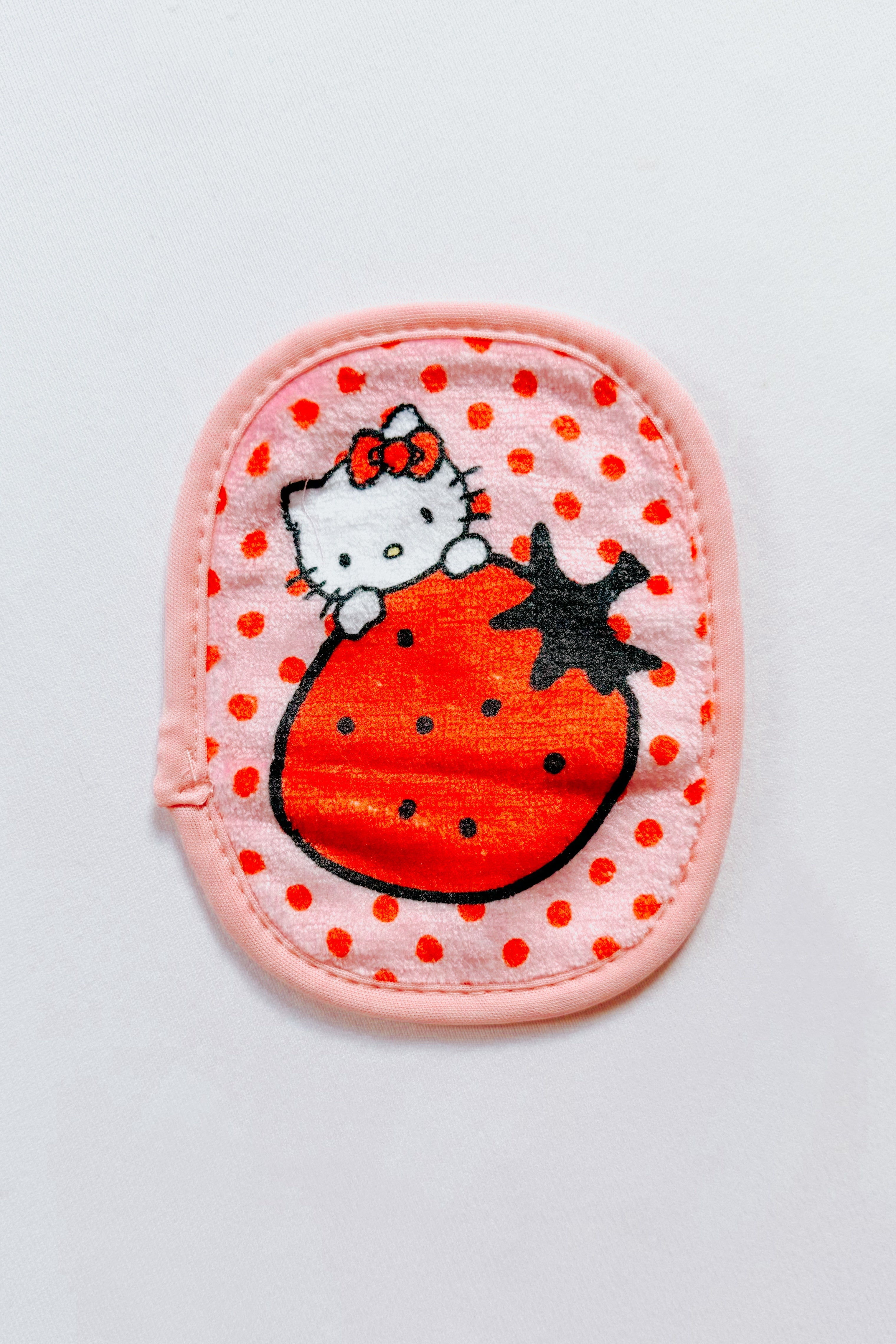 Small pink makeup eraser pad with red polka dots featuring a cute cartoon cat holding a large strawberry design
