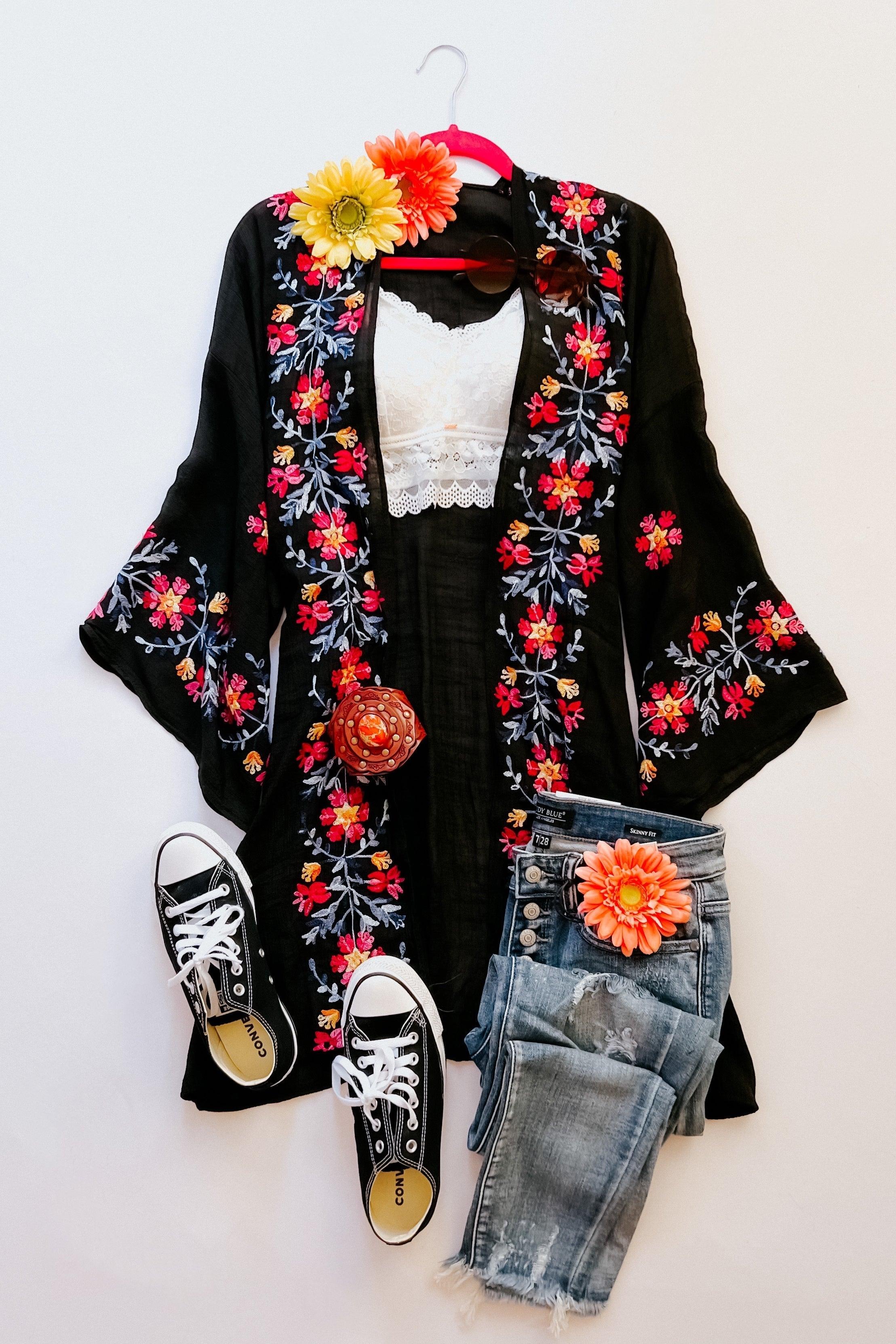 Black embroidered duster with vibrant floral patterns paired with distressed jeans, white lace top, and black canvas sneakers