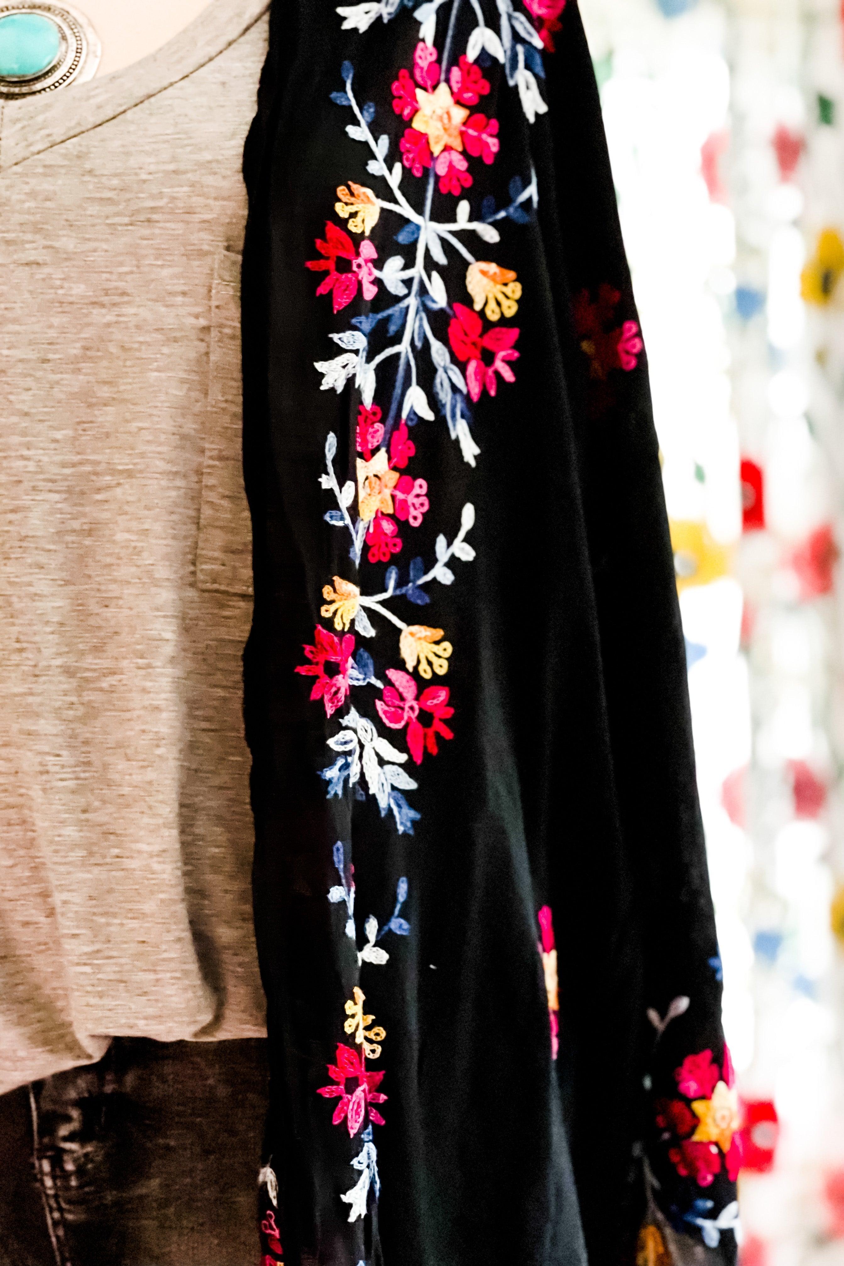 Close-up of a black embroidered duster sleeve with vibrant floral patterns worn over a beige top indoors