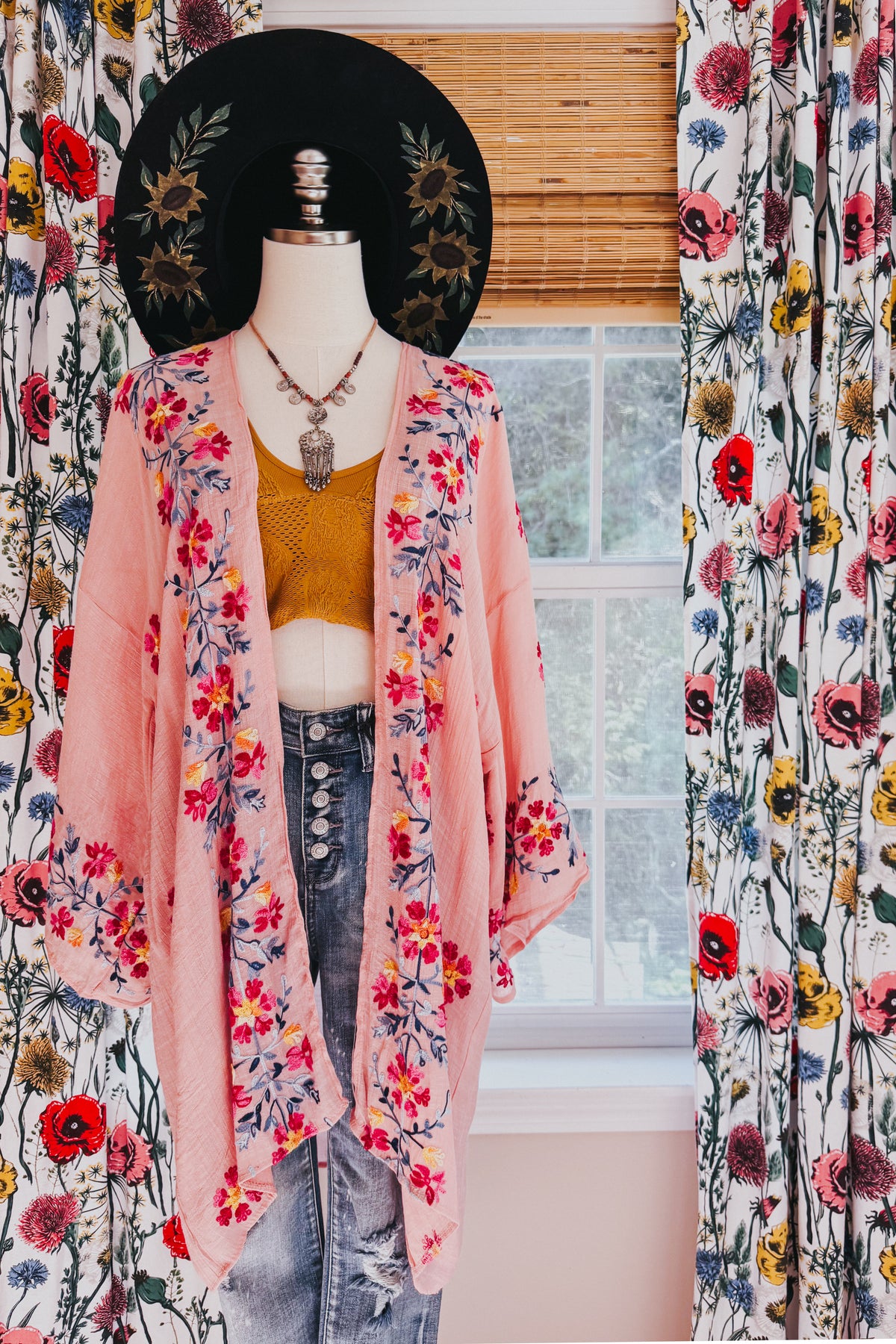 Rose floral embroidered duster layered over a mustard cropped top and distressed jeans on a mannequin in a bright room