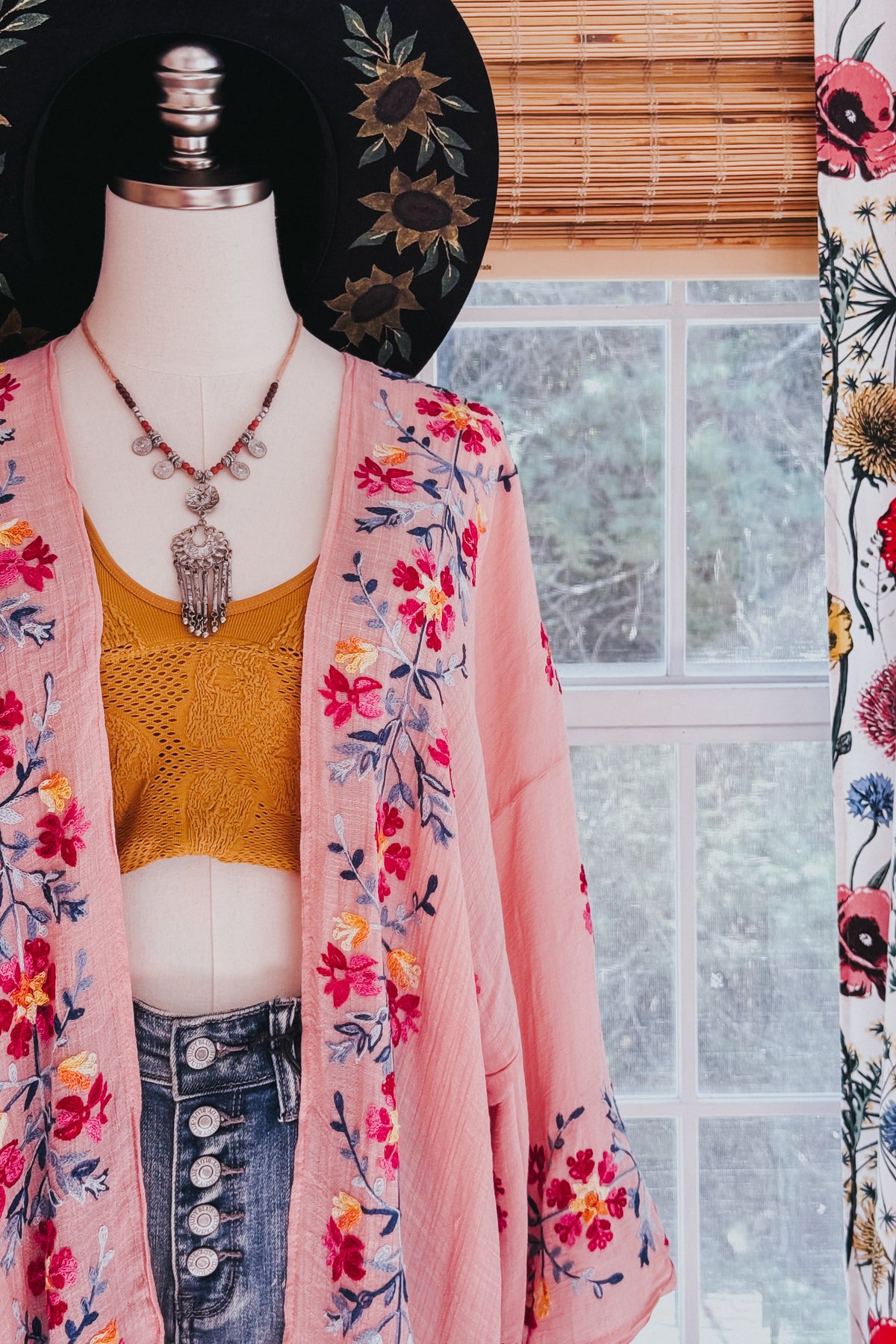 Rose floral embroidered duster layered over a mustard crochet top and high waist jeans on a mannequin indoors