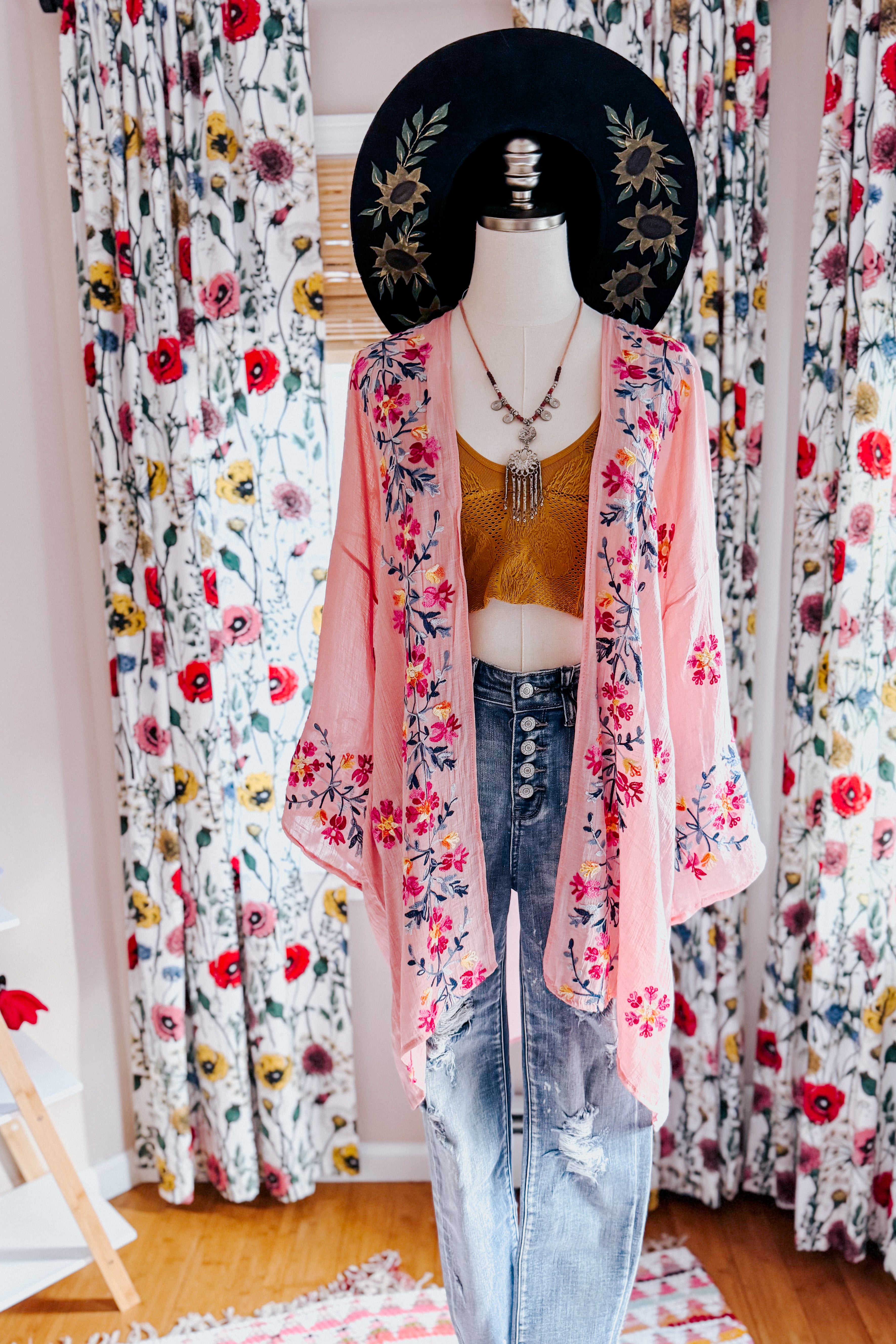 Mannequin dressed in a rose embroidered duster layered over a mustard crop top and distressed high-waisted jeans indoors