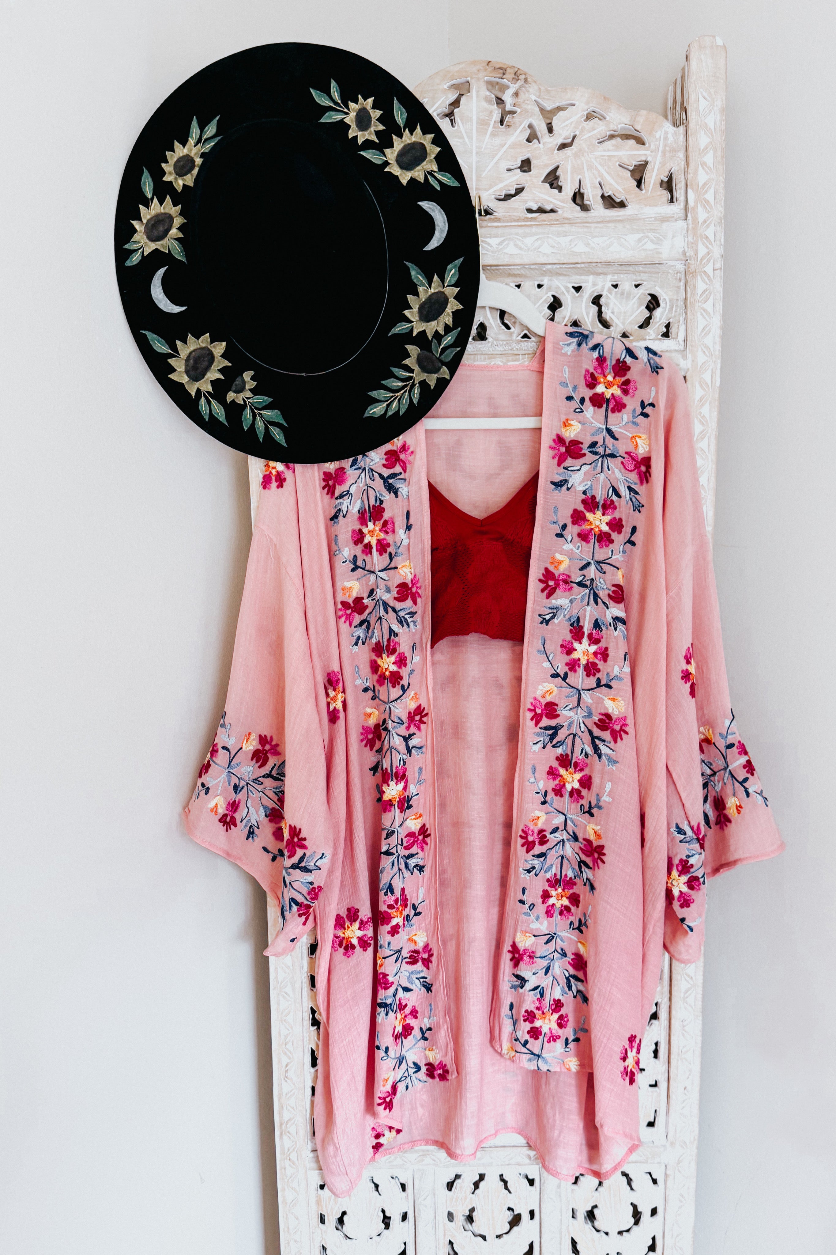 Rose pink duster with vibrant floral embroidery layered over a red top, paired with a black hat featuring sunflower and moon designs