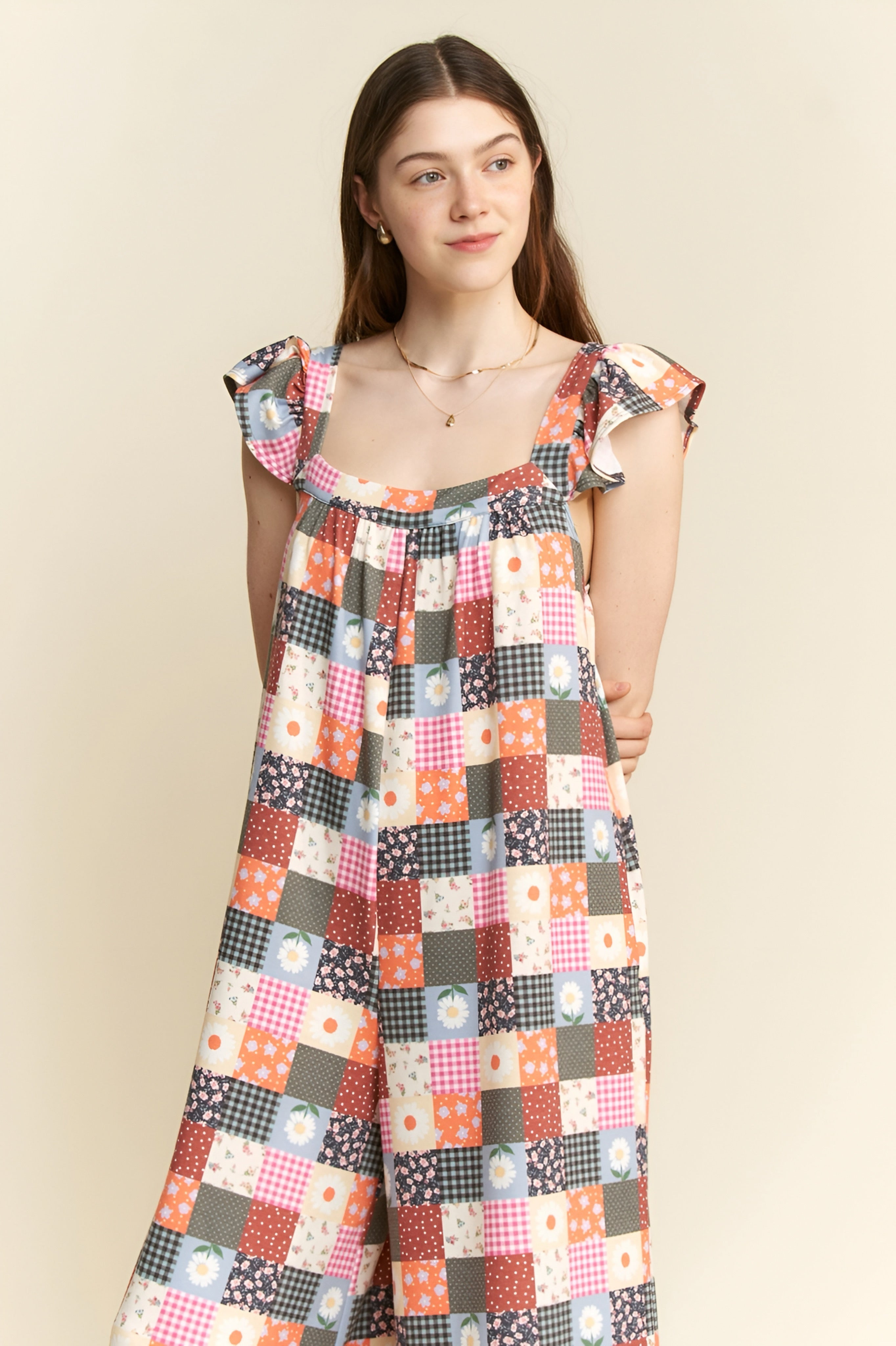 Woman wearing a multicolor patchwork jumpsuit with ruffle sleeves posing against a beige backdrop
