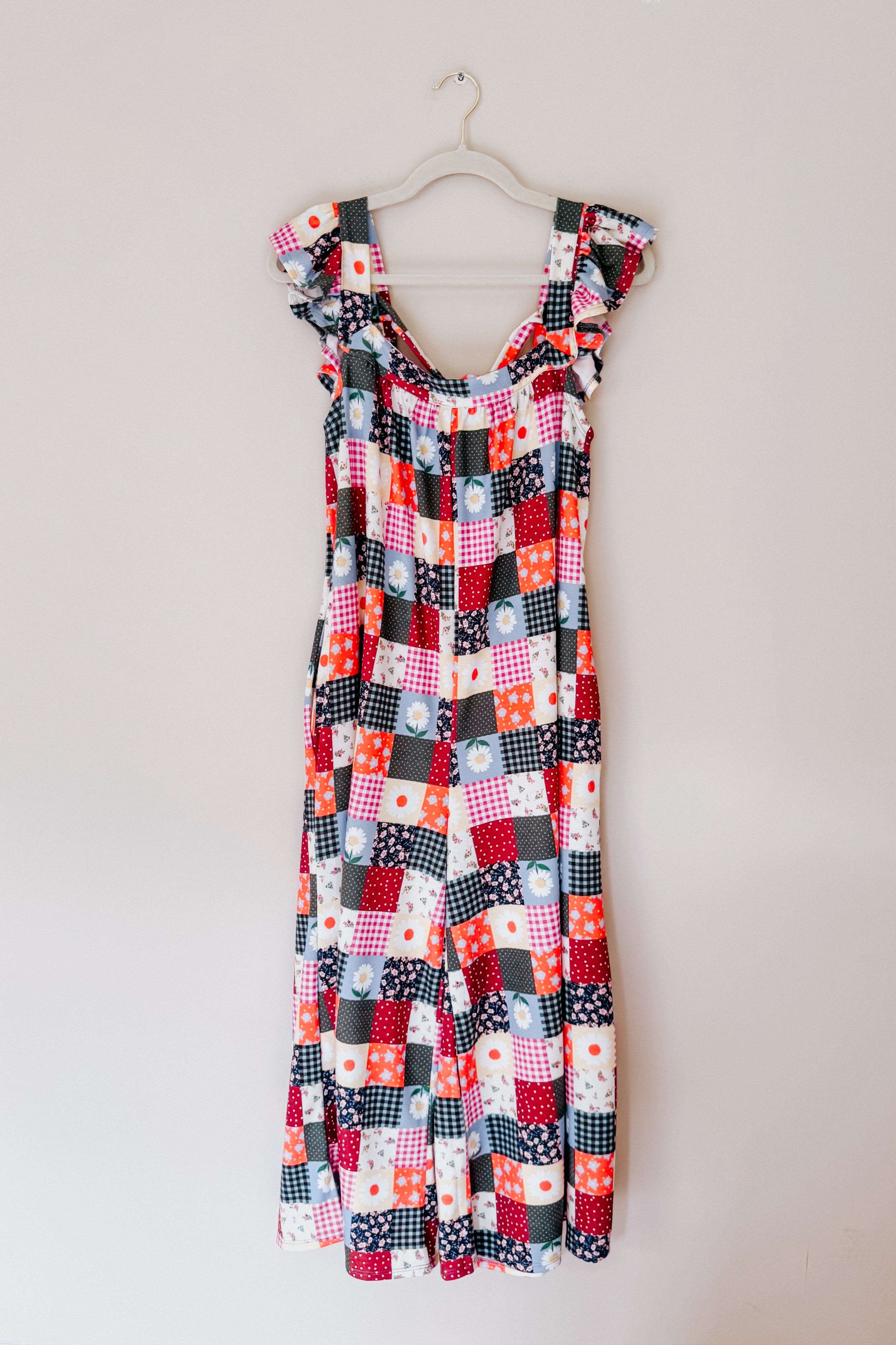 Multicolor patchwork jumpsuit with ruffle sleeves and floral and gingham patterns hanging against a pale wall