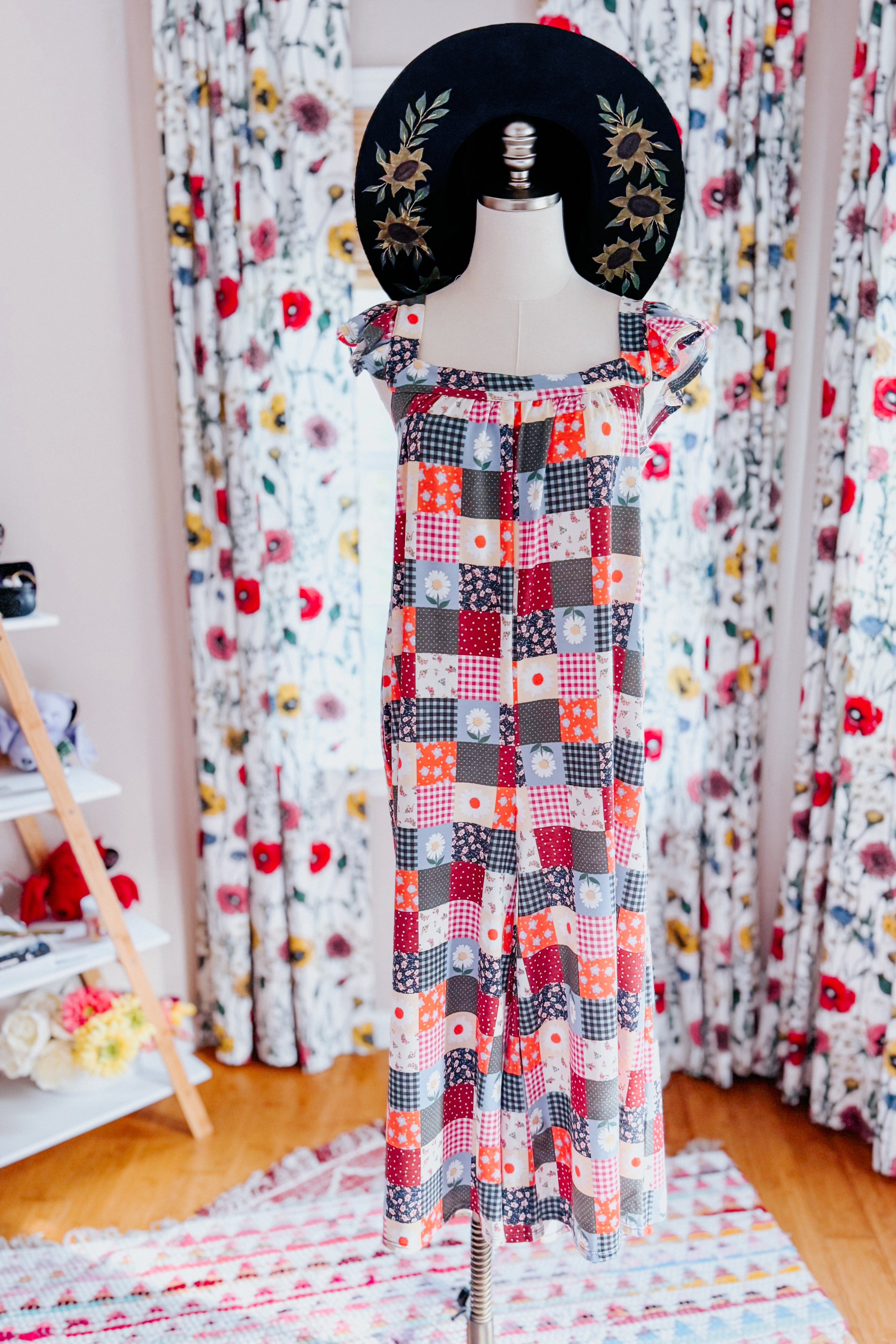 Patchwork jumpsuit with ruffle sleeves in multicolor pattern styled with wide-brim hat featuring floral embroidery indoors