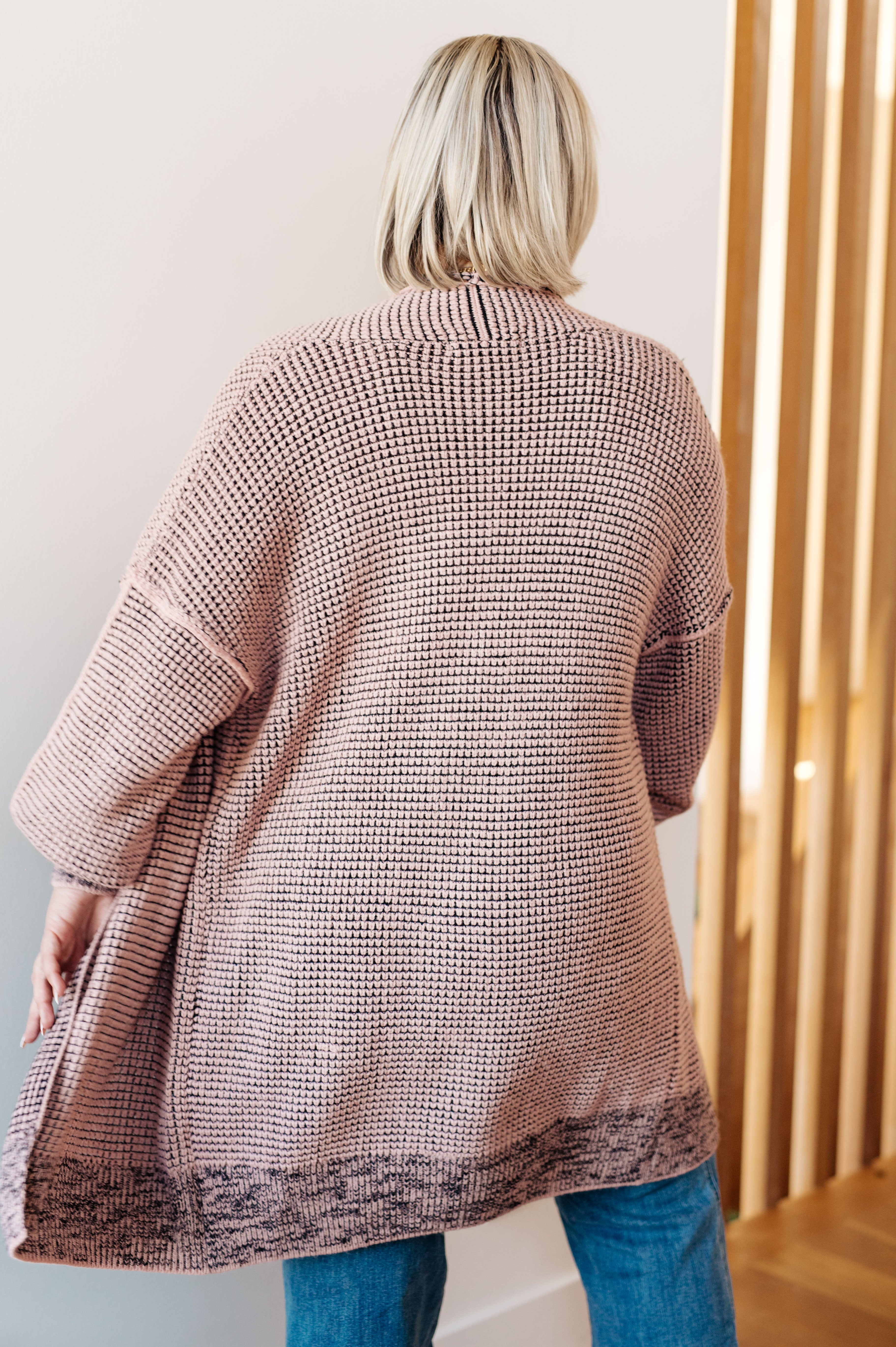 Back view of person wearing a loose mauve knit cardigan with patterned hem, paired with blue jeans indoors