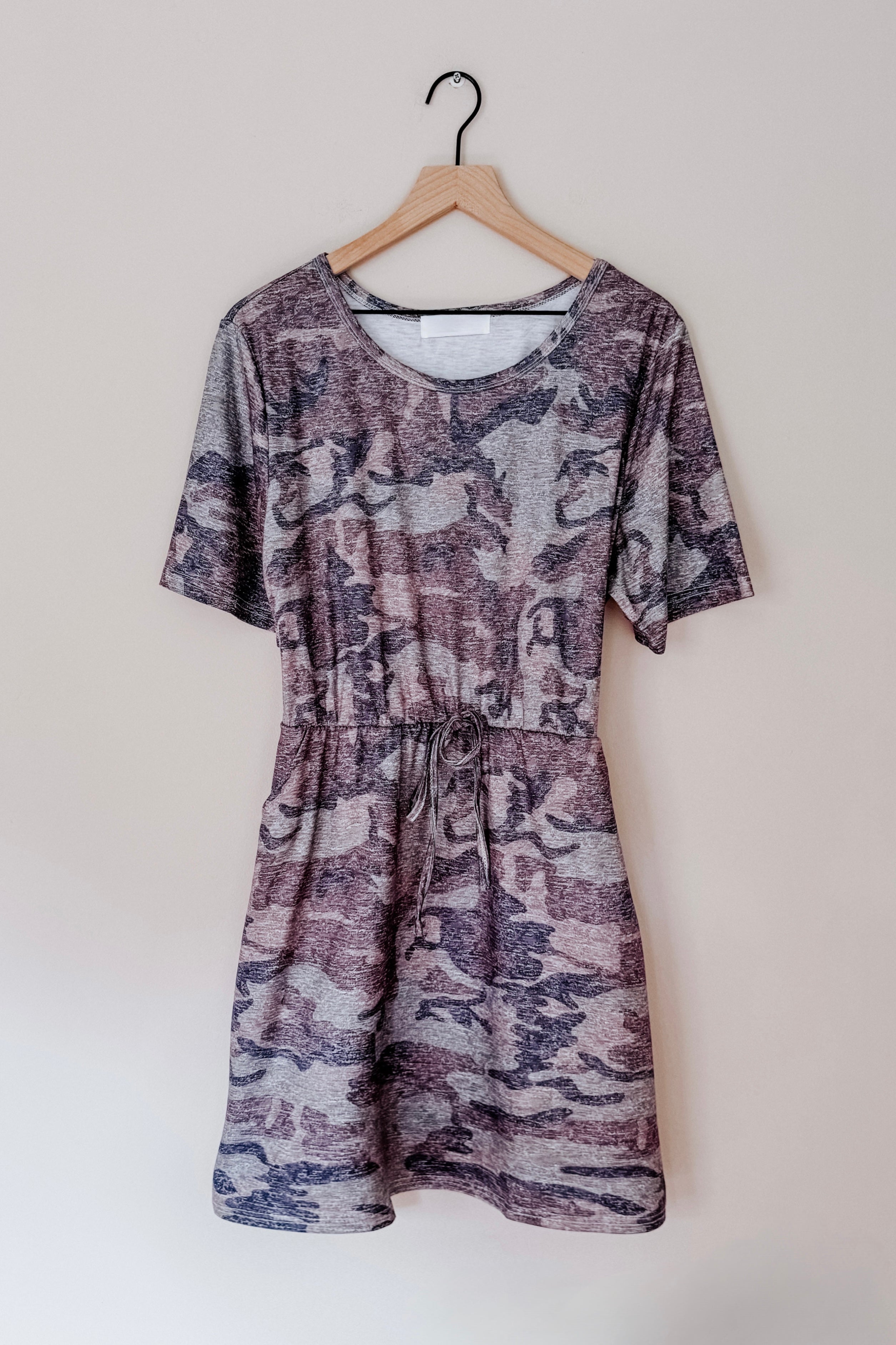 Blue vintage camo print dress with short sleeves and a drawstring waist hanging on wooden hanger against beige wall
