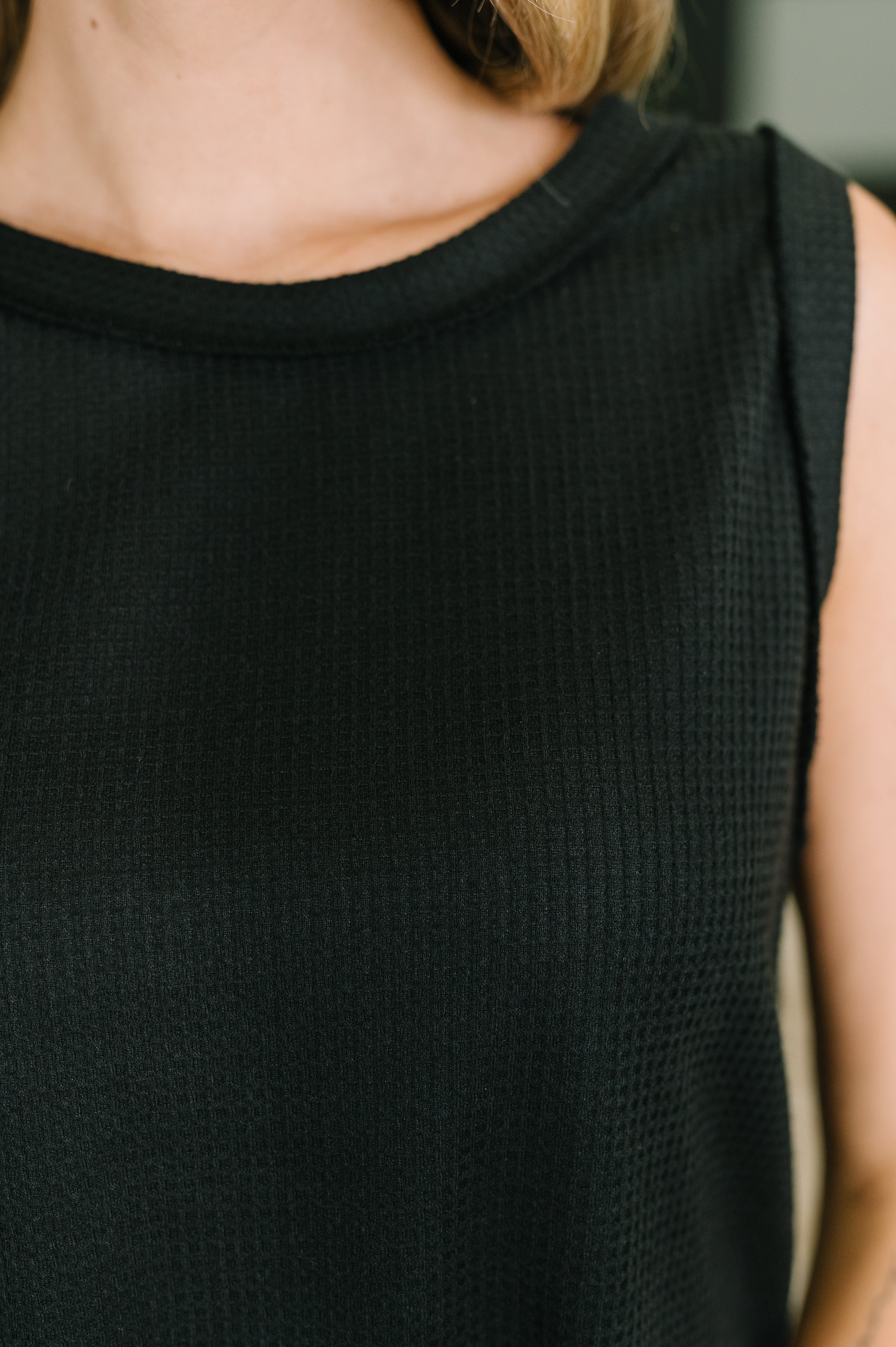 Close-up of black waffle knit sleeveless top with banded neckline and exposed seam details on model's upper torso