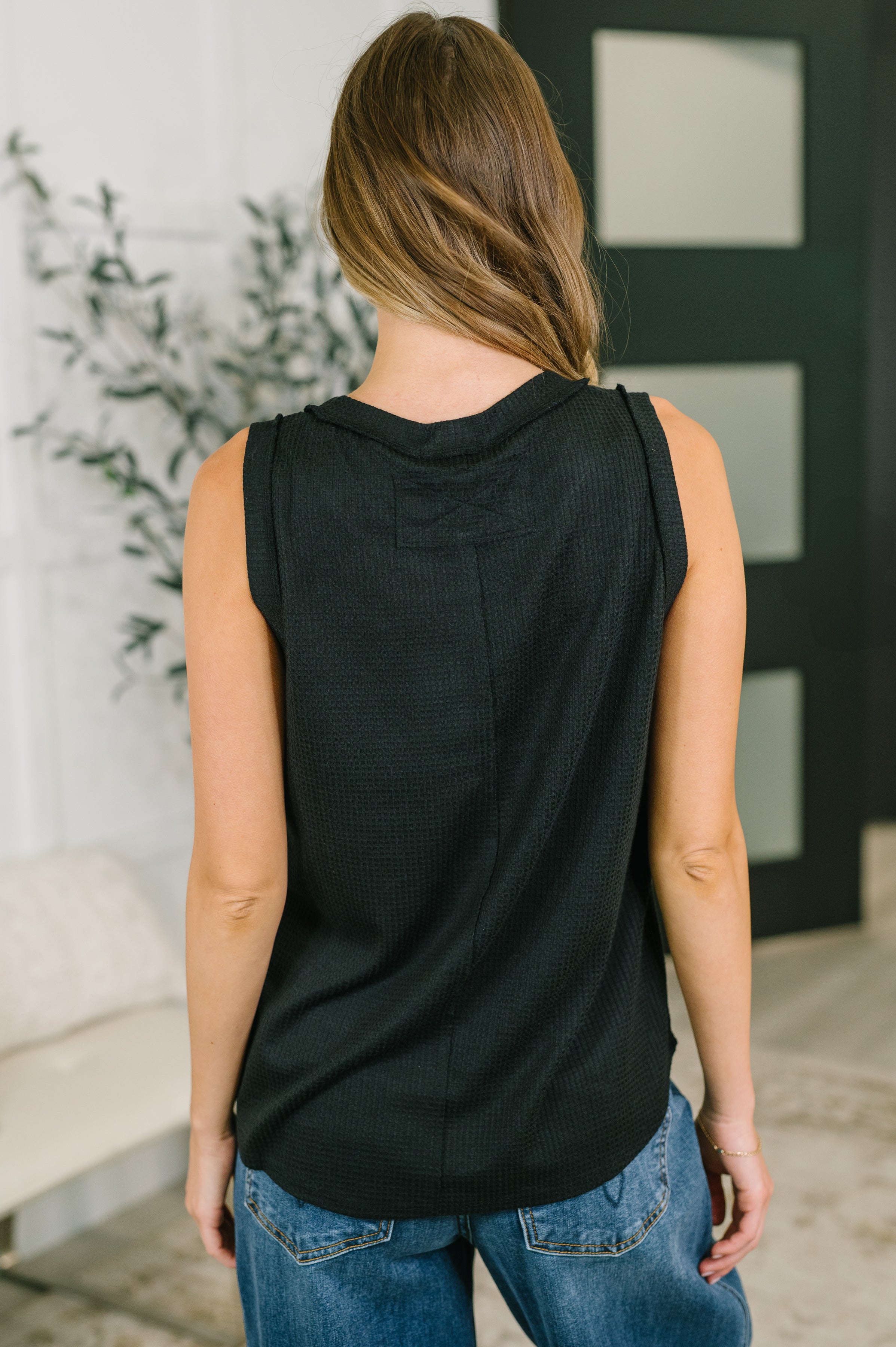 Back view of woman wearing black textured sleeveless tank with round neckline and exposed seam details indoors