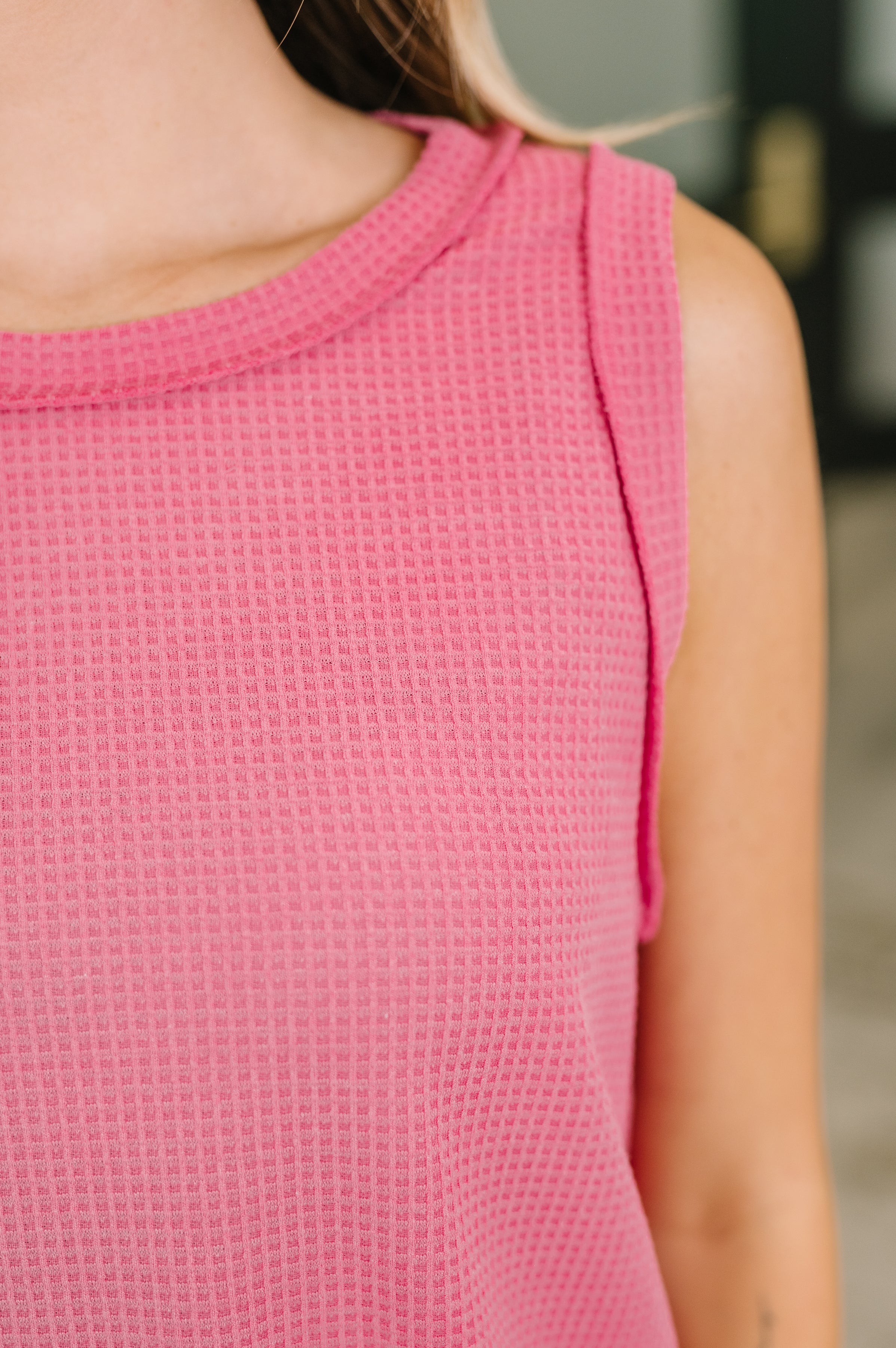 Close-up of pink waffle knit sleeveless tank with banded round neckline and exposed seam detail on upper torso