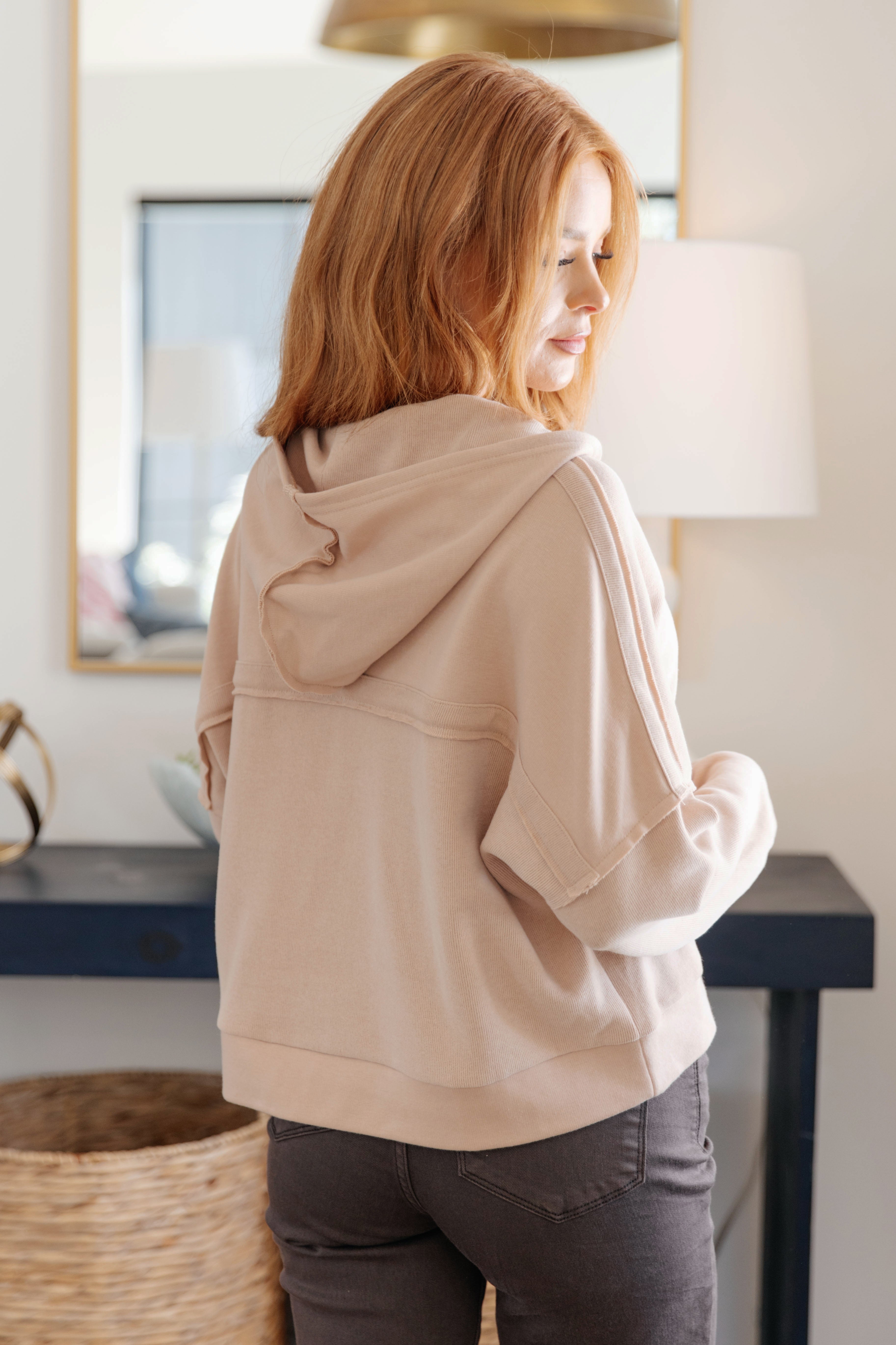Woman with red hair wearing a beige hoodie styled casually in a bright room with cozy home decor background