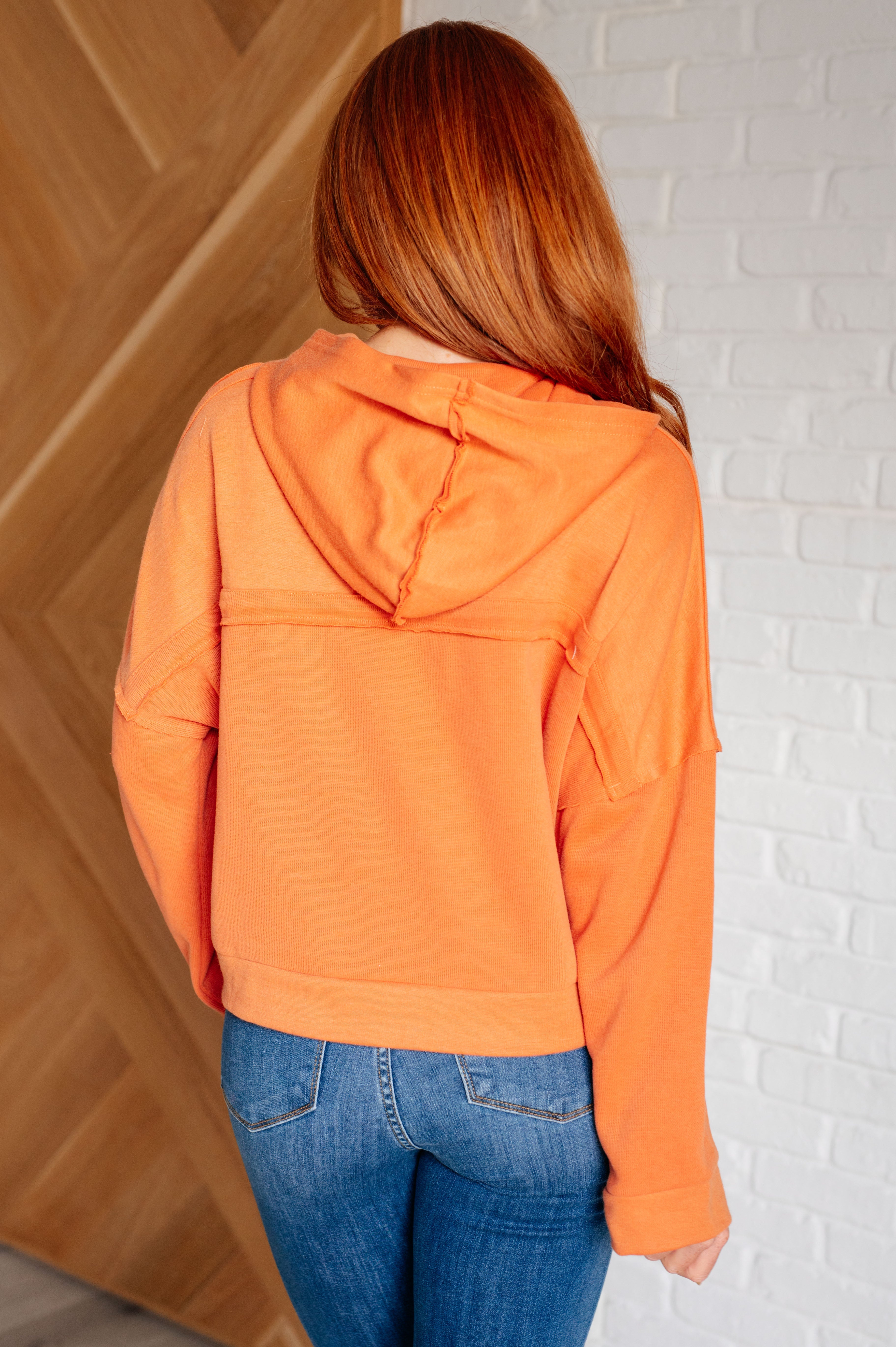 Woman with long red hair wearing an orange relaxed-fit hoodie paired with blue jeans in a cozy indoor setting