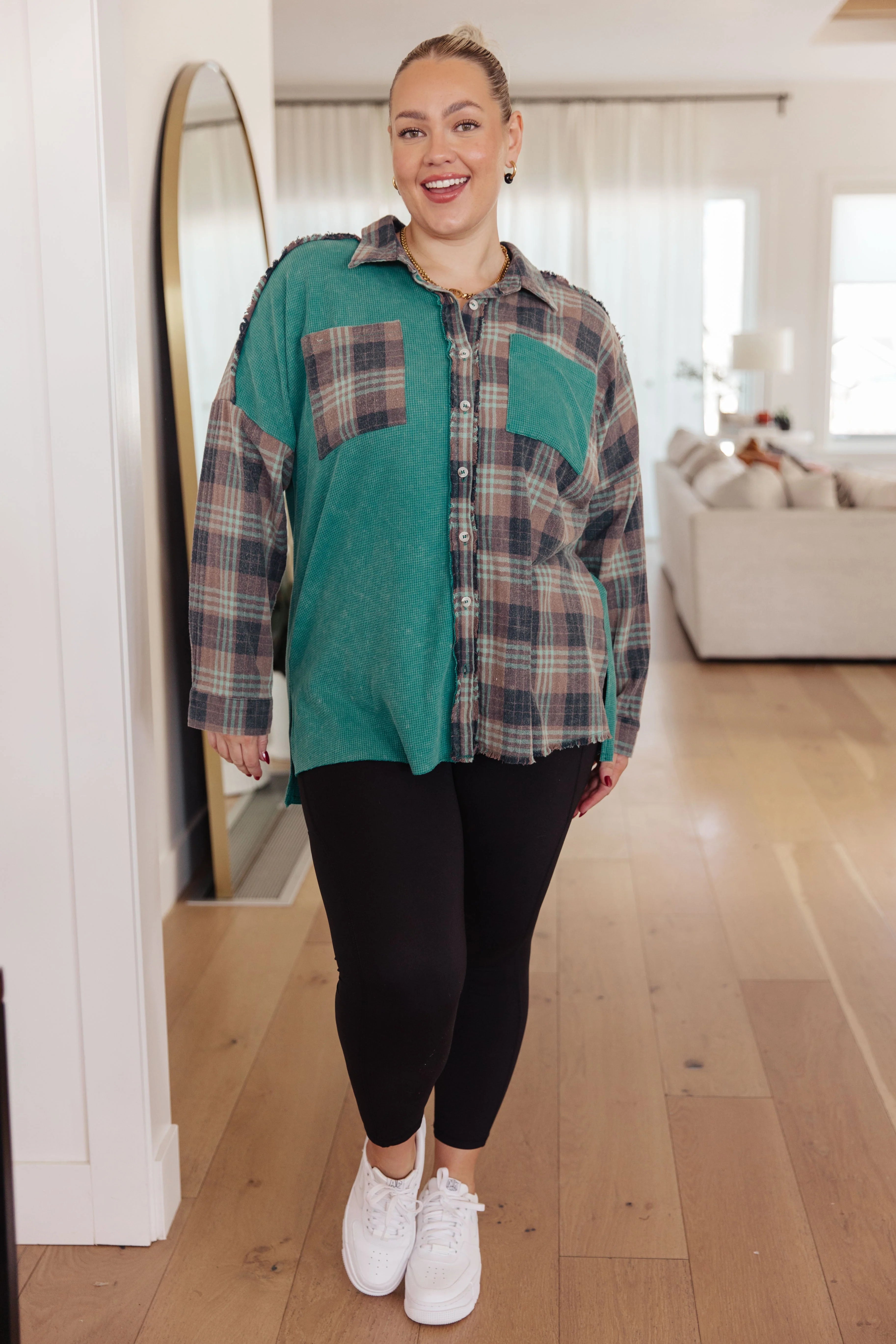 Plus-size woman smiling wearing a teal and plaid thermal button-up paired with black leggings and white sneakers indoors