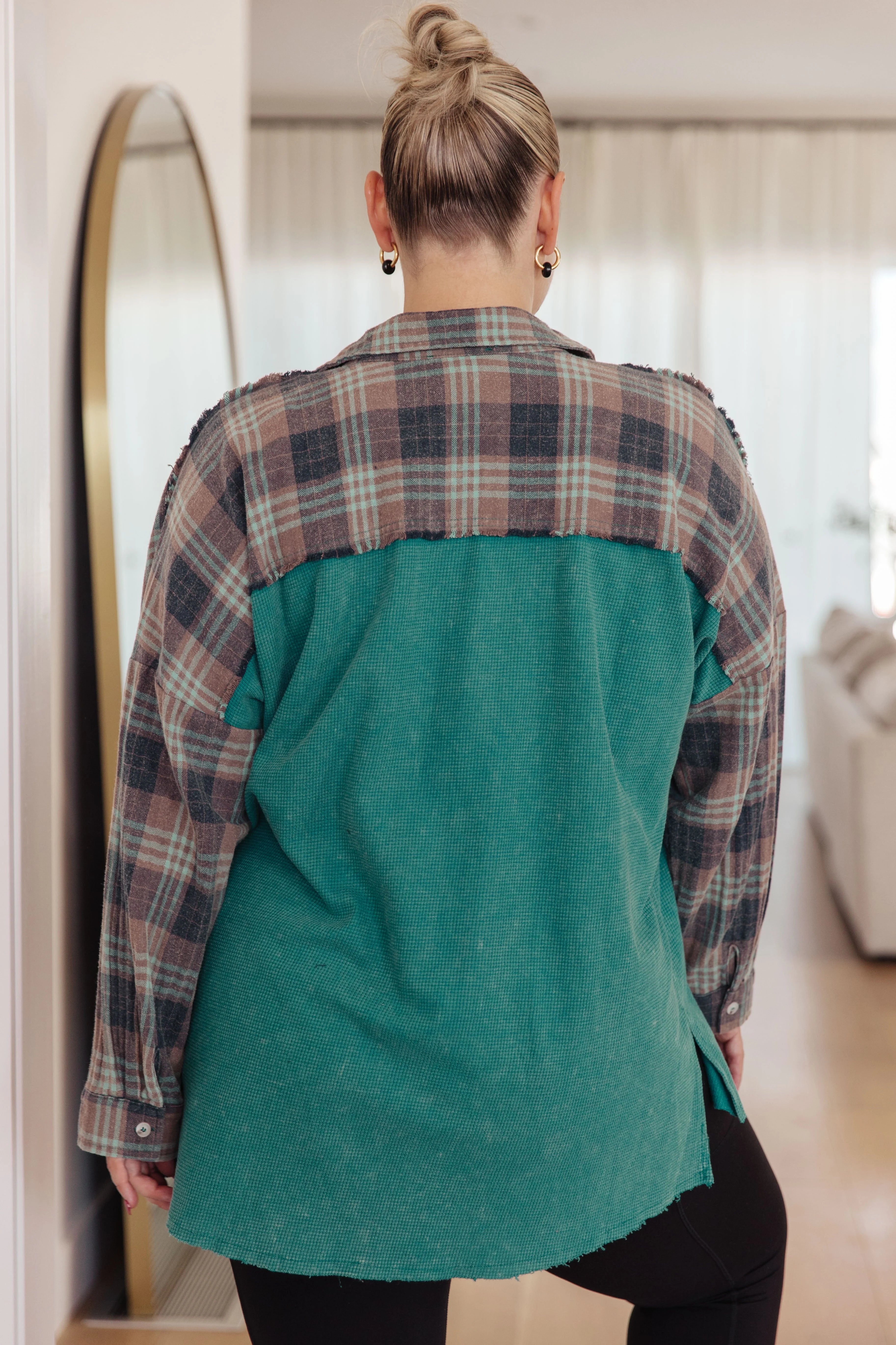 Woman wearing a teal thermal shirt with plaid yoke and sleeves standing indoors with hair in a bun