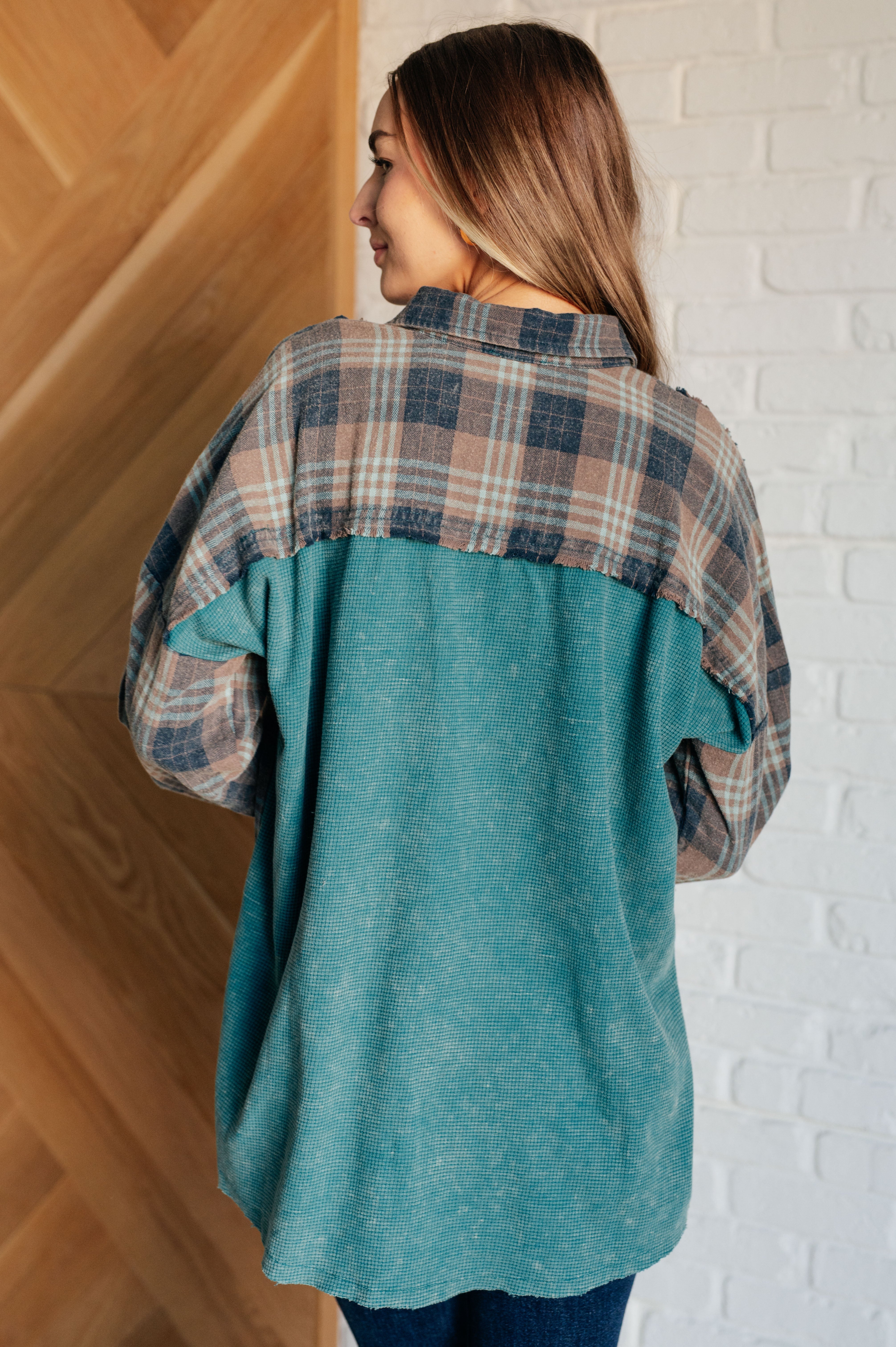 Woman wearing a teal thermal shirt with plaid button-up detail on shoulders, standing indoors with back facing camera