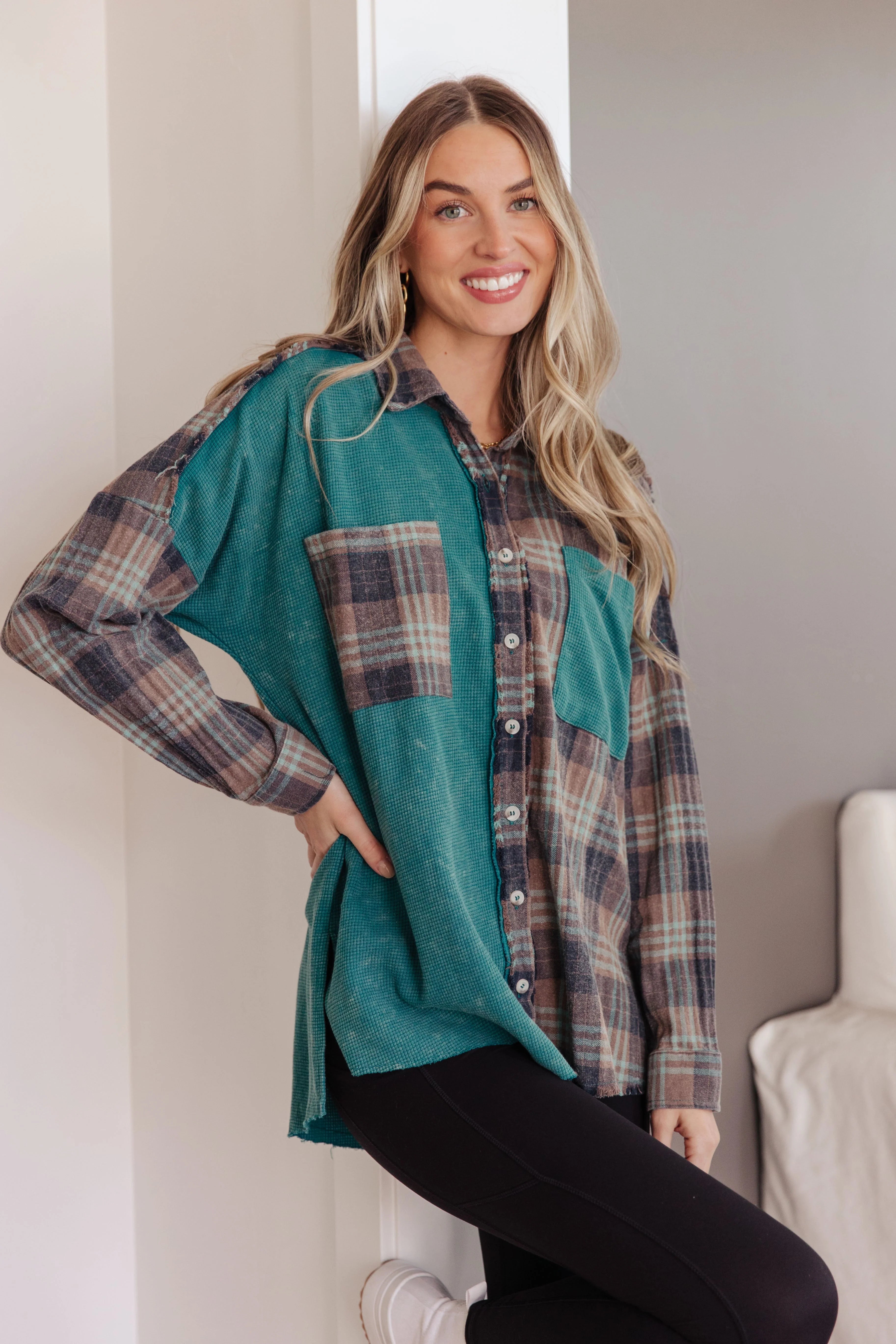 Smiling woman wearing a teal and brown plaid thermal button-up with pockets, paired with black leggings indoors