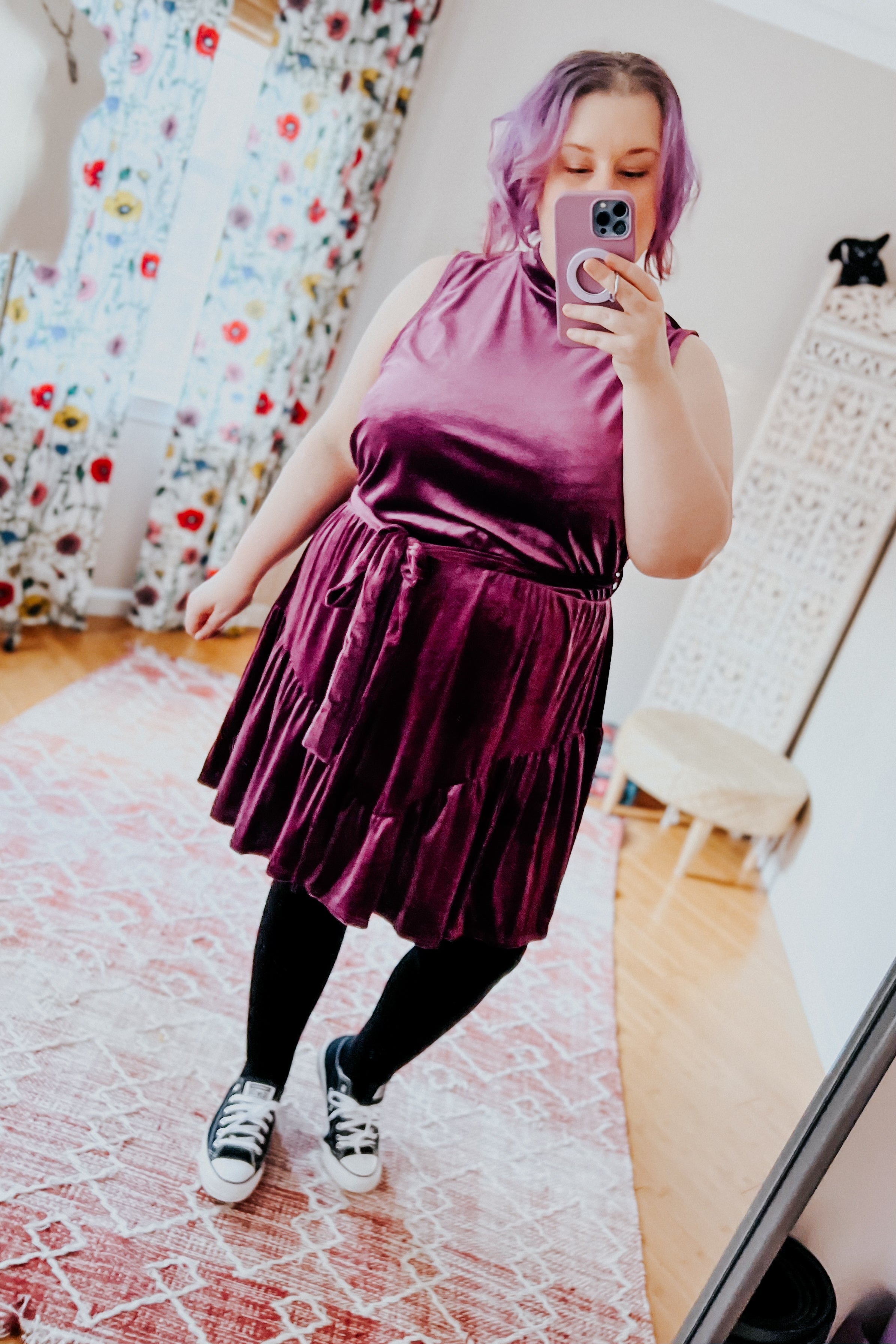 Plus-size woman taking mirror selfie wearing a purple velvet dress with bow detail paired with black tights and sneakers