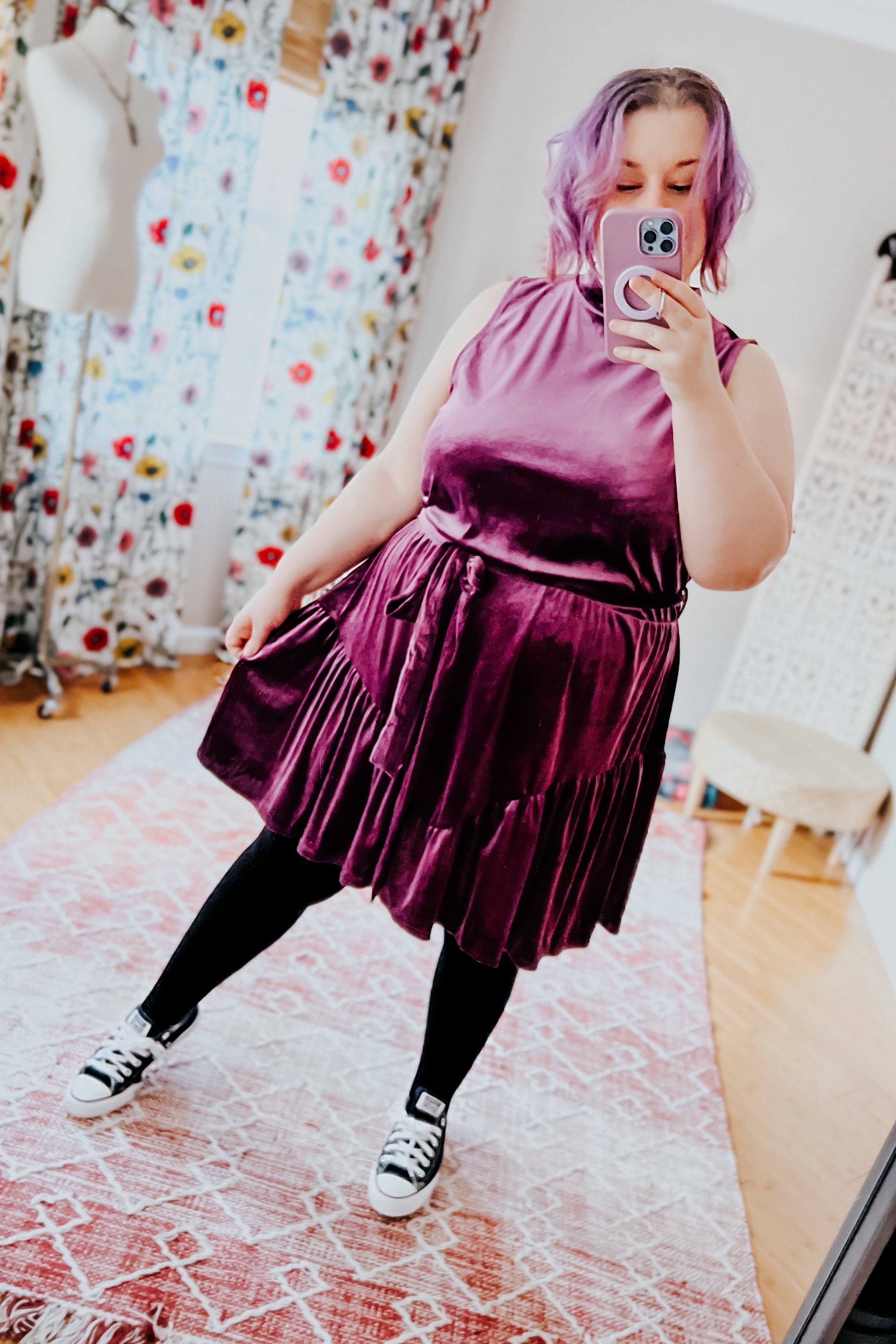 Plus-size woman with purple hair wearing a plush purple velvet dress styled with black leggings and sneakers indoors