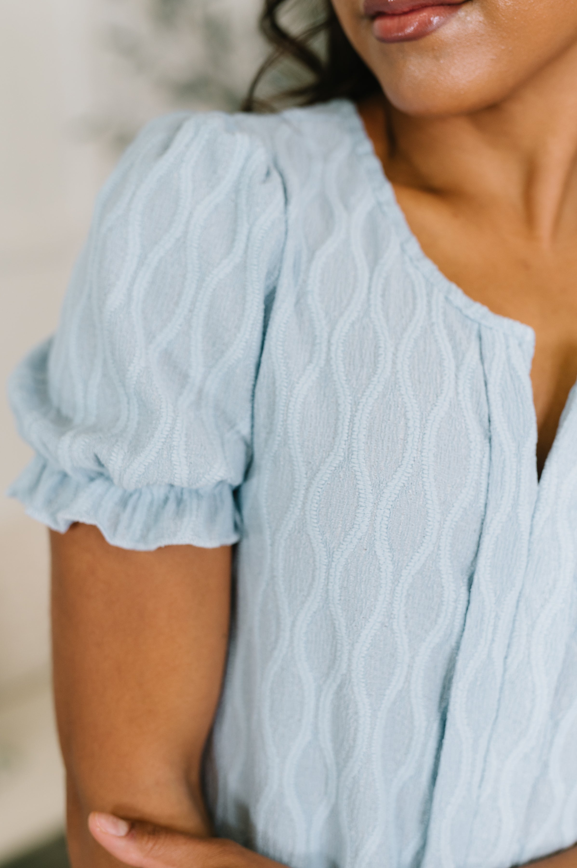 Close-up of powder blue textured blouse with puffed sleeves and delicate ruffled cuffs on a model's arm