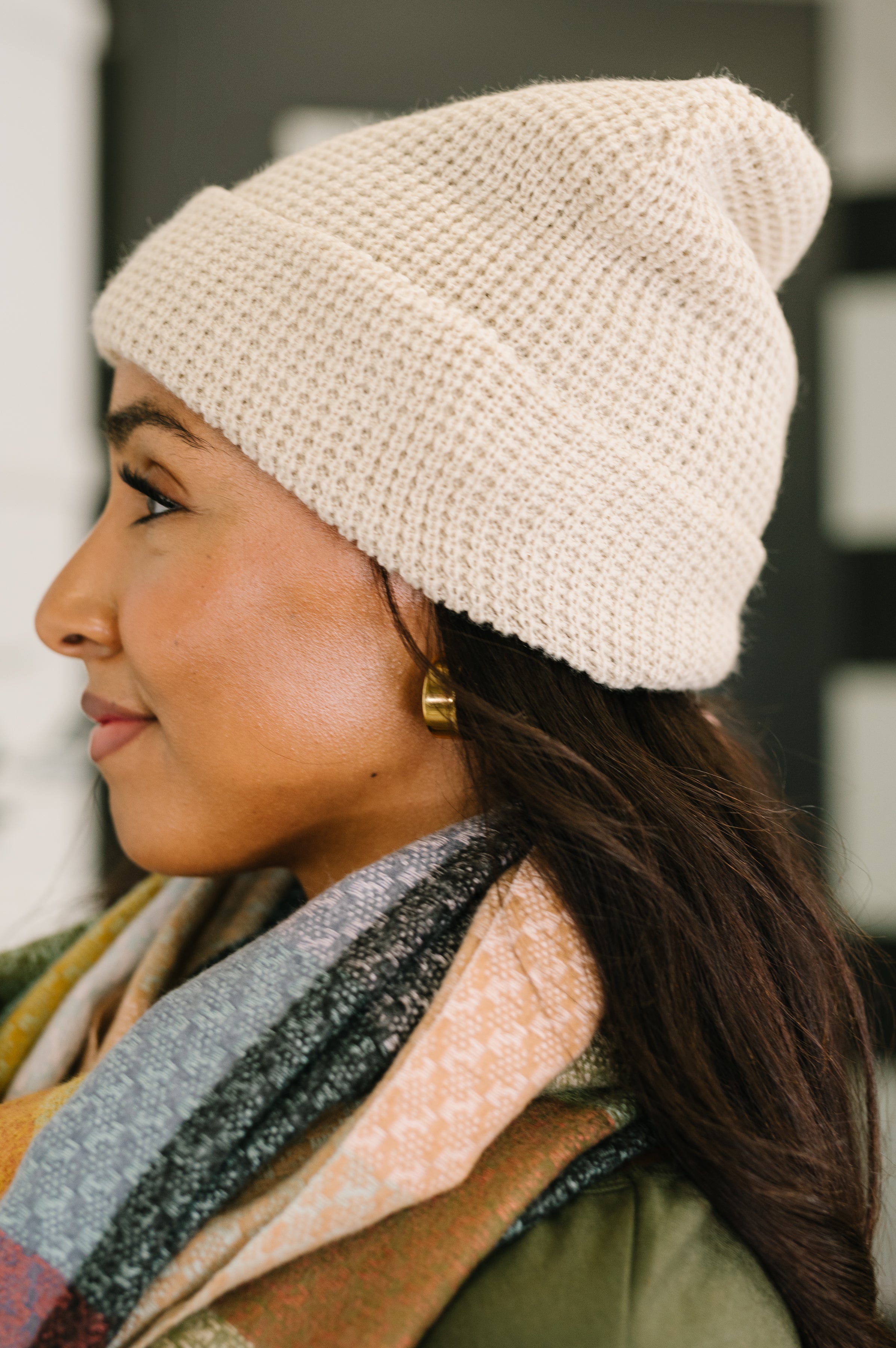 Profile of woman wearing a beige waffle knit beanie with a colorful patterned scarf and gold hoop earring