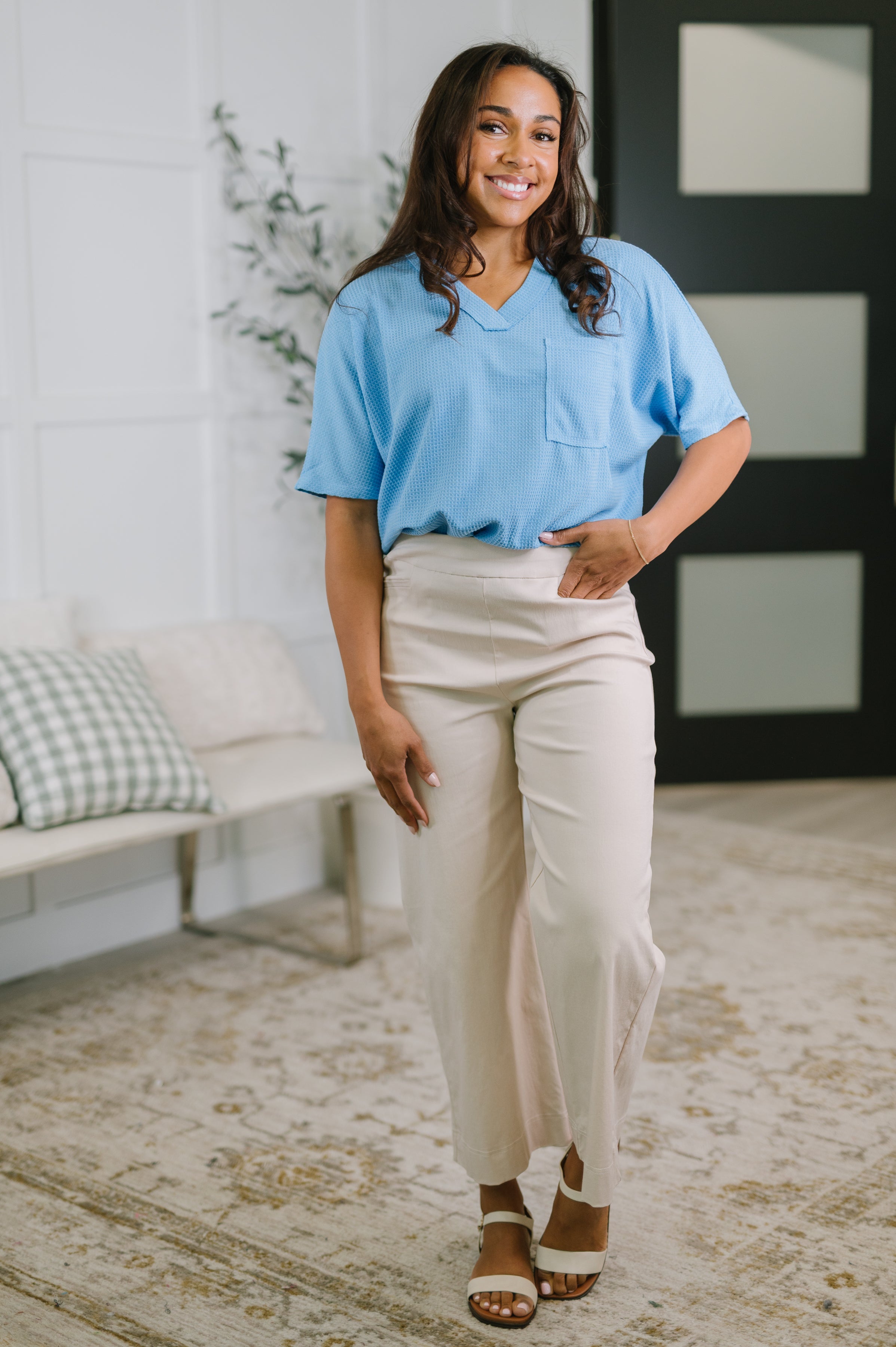 Woman wearing ocean blue relaxed v-neck tee with chest pocket paired with light beige wide-leg pants indoors