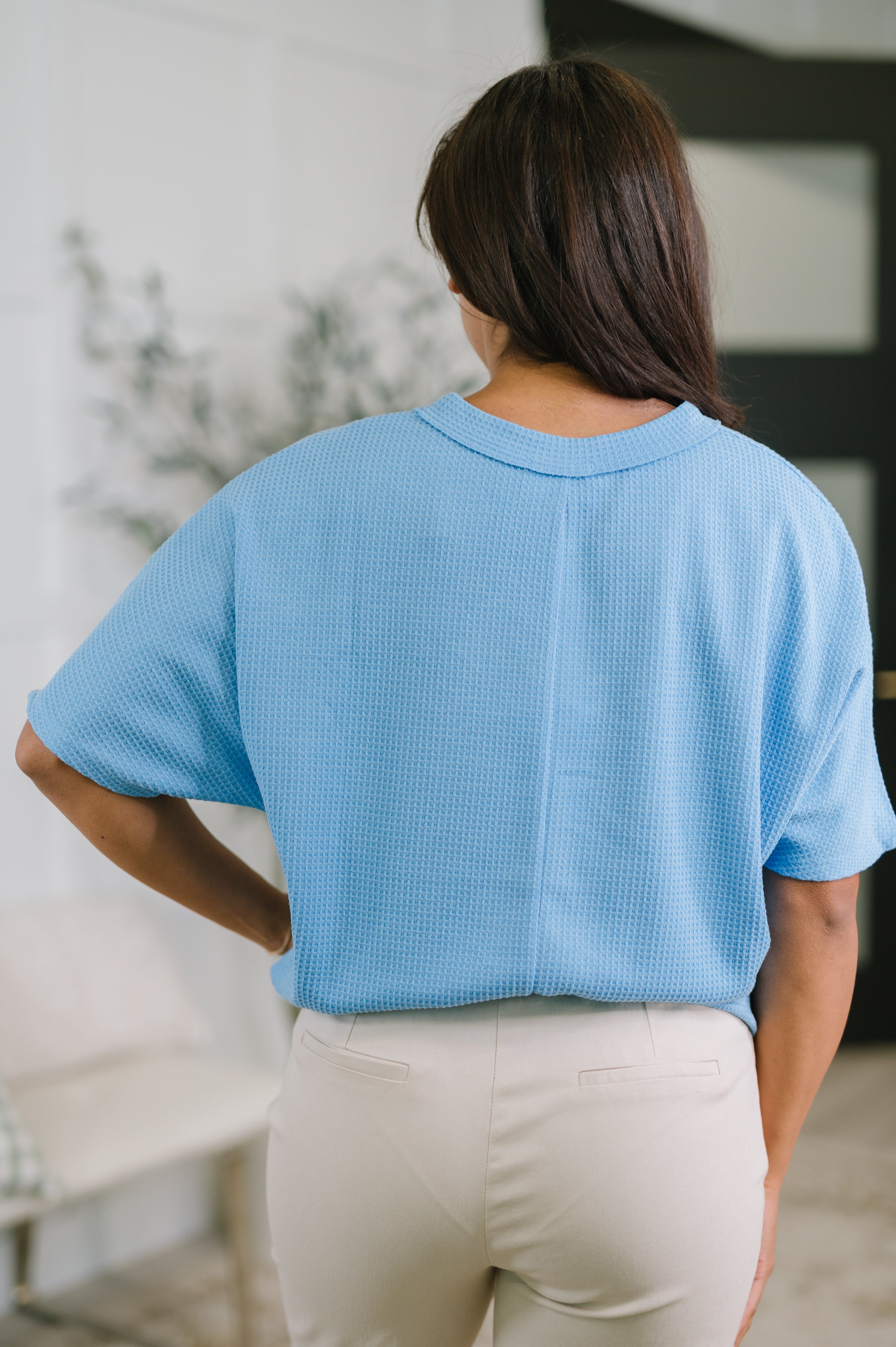 Back view of woman wearing ocean blue textured basic v-neck tee with relaxed fit and light beige pants indoors
