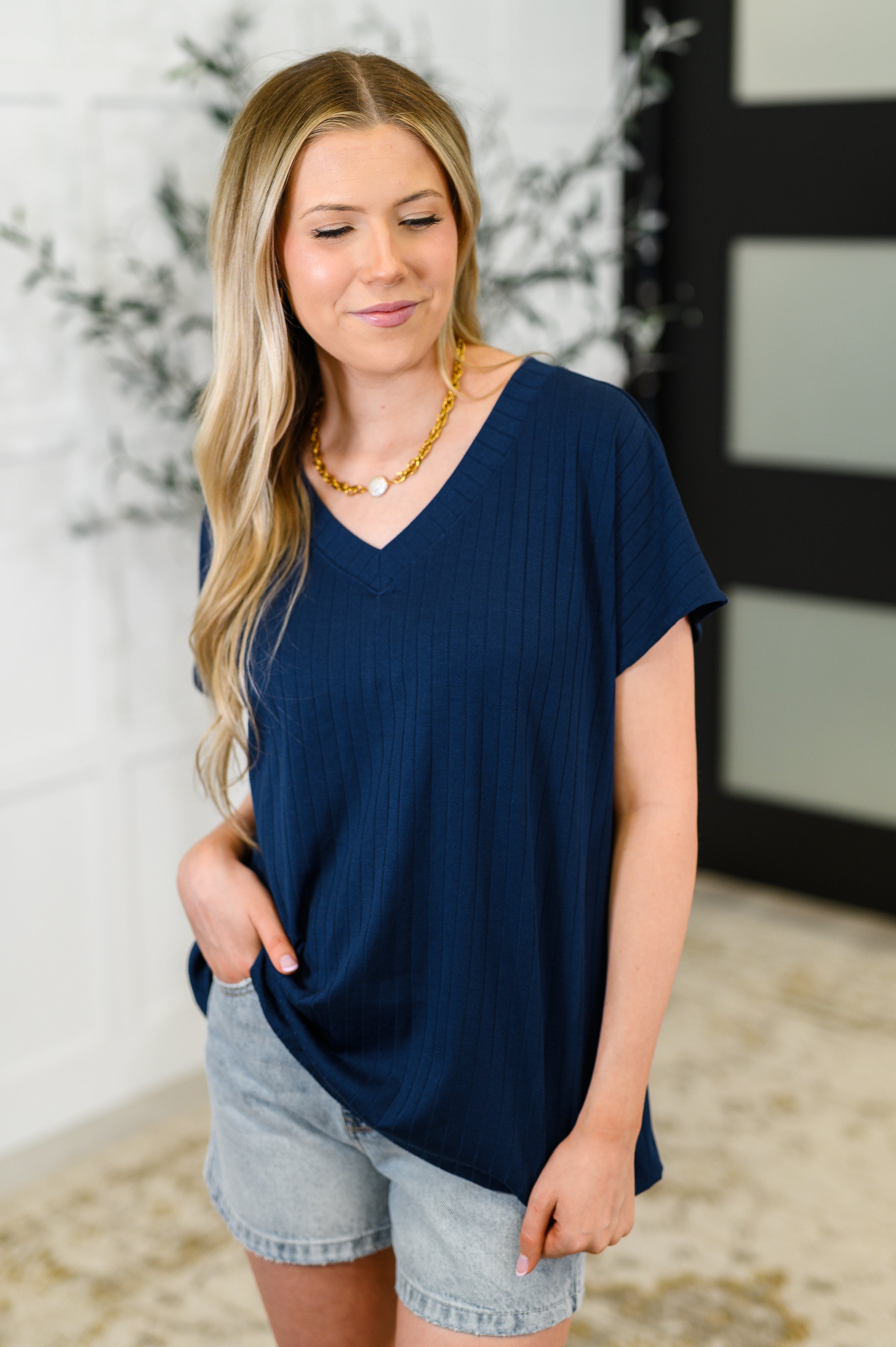 Woman wearing navy ribbed V-neck top paired with light denim shorts and a gold necklace indoors