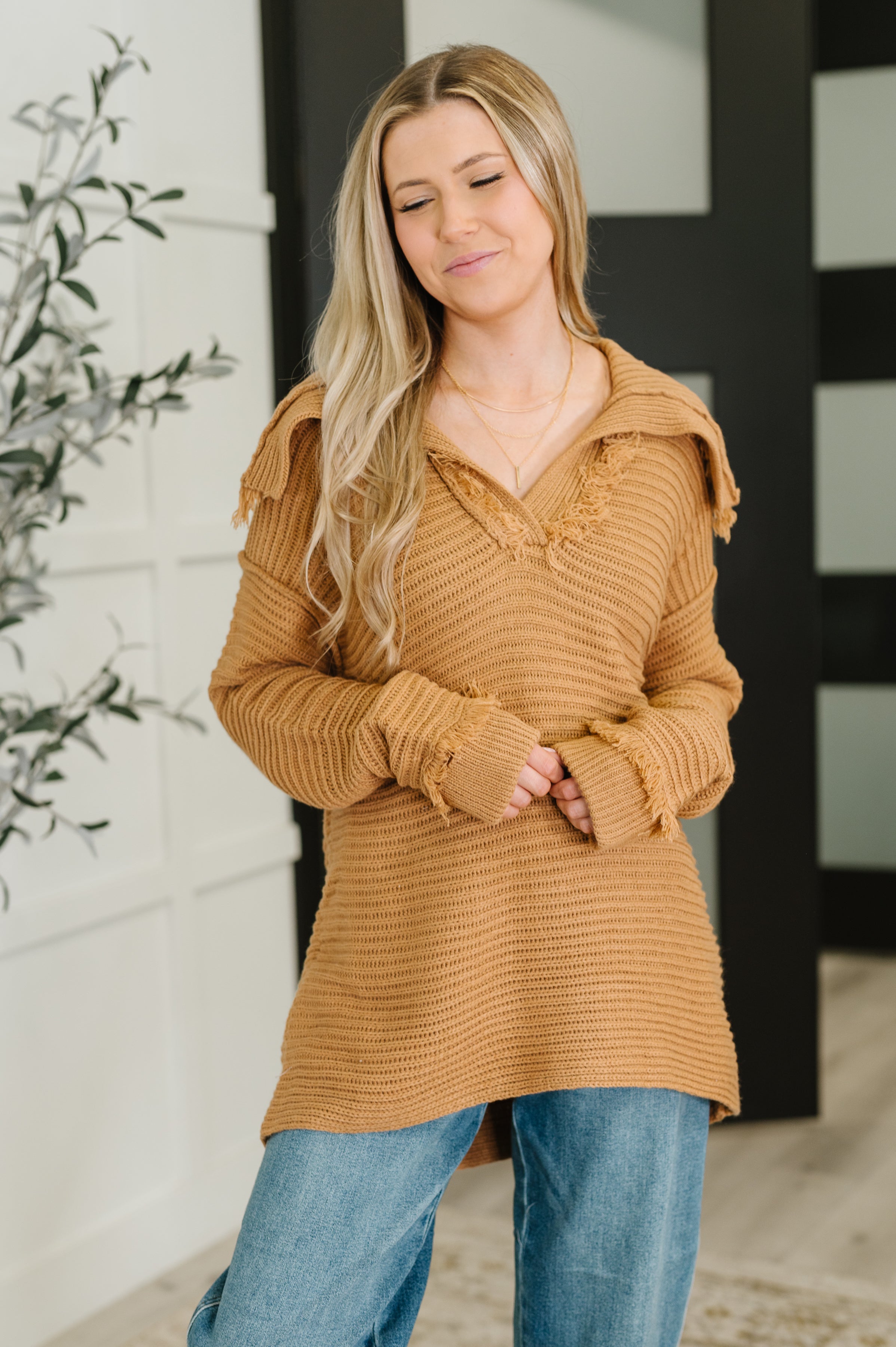 Woman wearing a camel knit sweater with distressed details paired with relaxed blue jeans indoors
