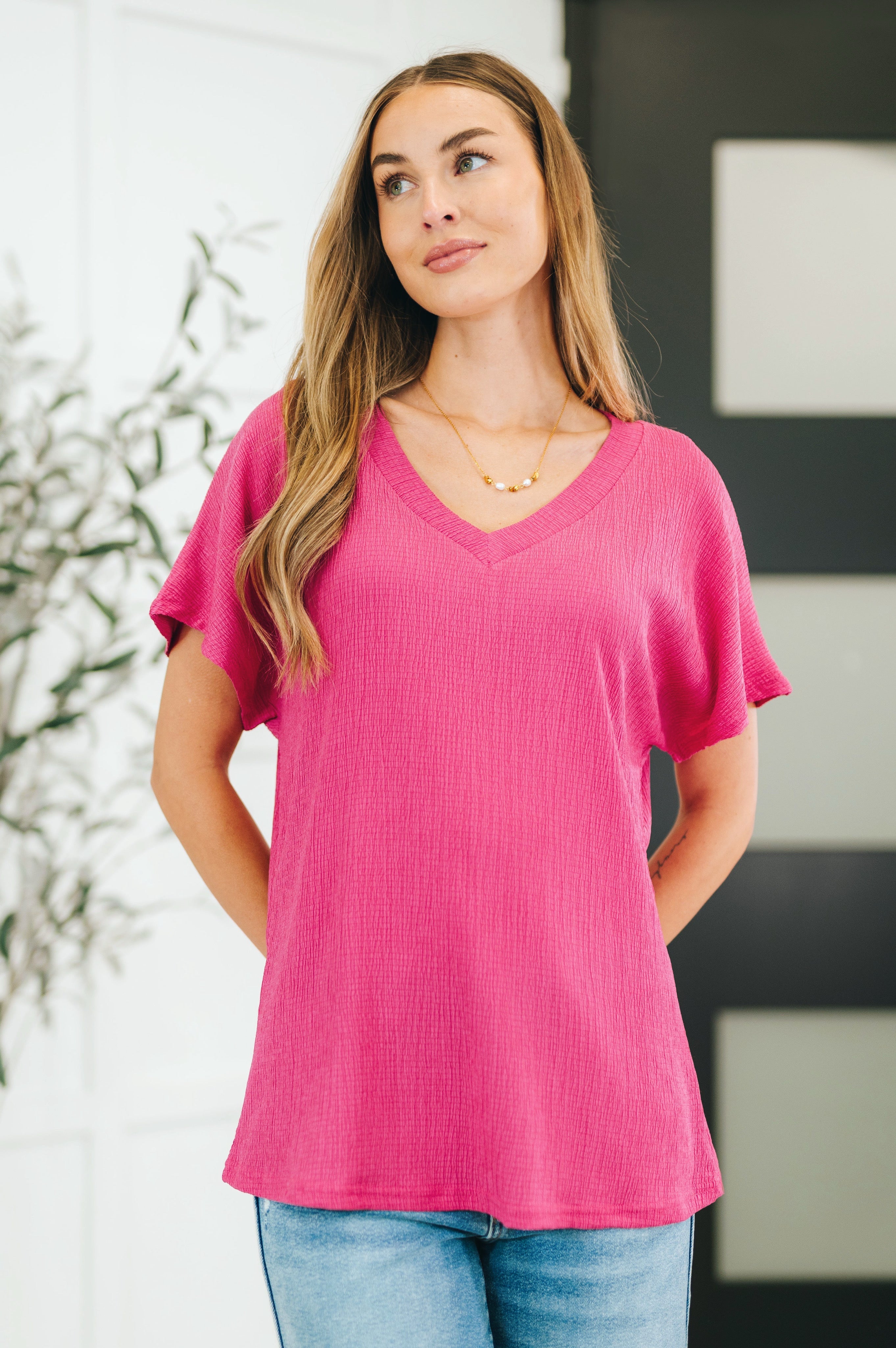 Woman wearing a magenta textured V-neck blouse with short sleeves paired with light wash jeans indoors