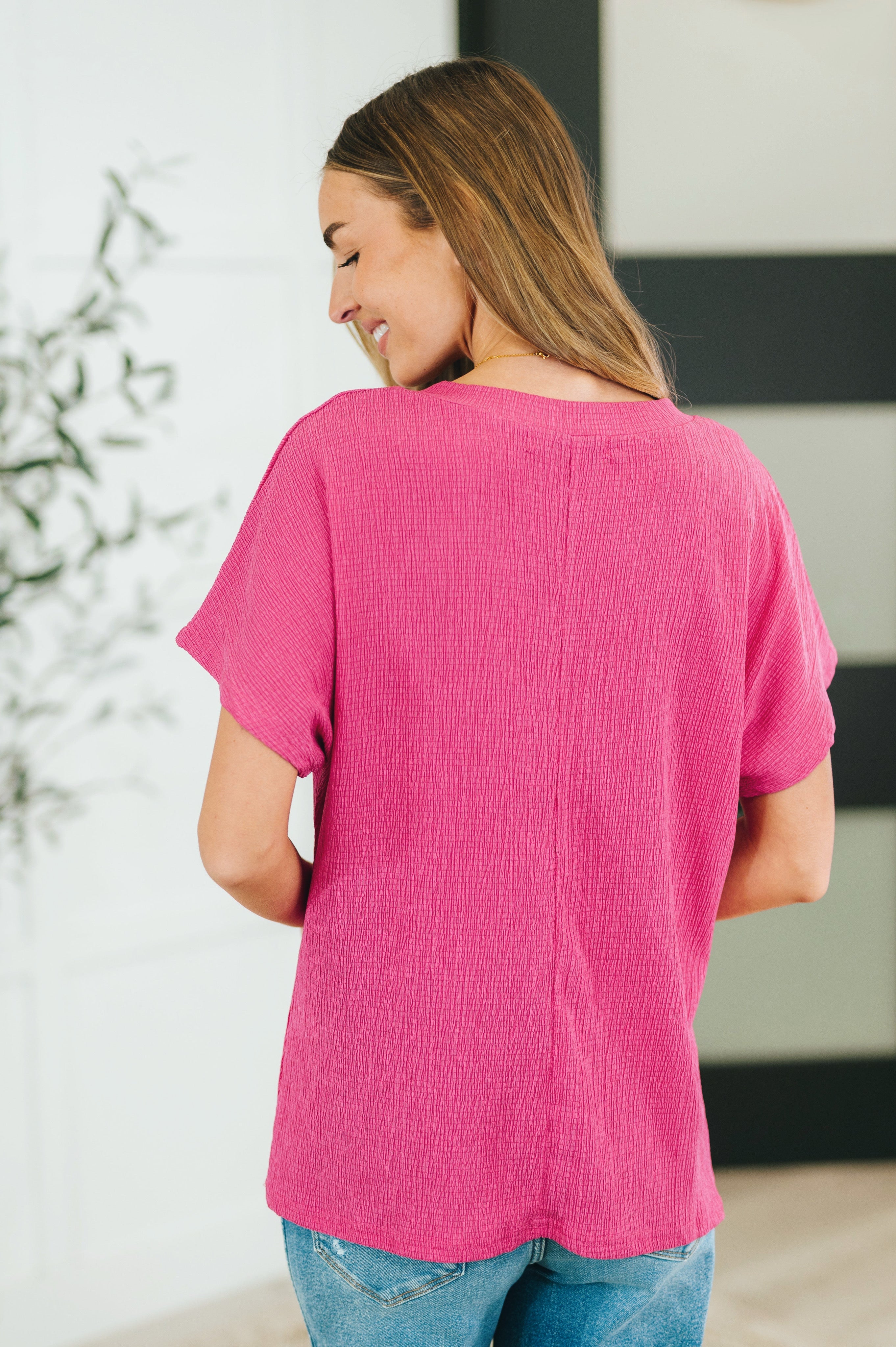 Woman wearing a magenta textured short-sleeve blouse with a relaxed fit and casual blue jeans indoors