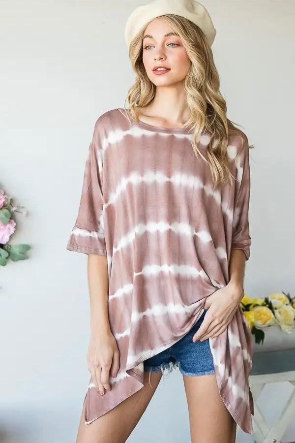 Woman wearing a pink striped tie dye tunic paired with denim shorts and a cream beret in a bright room