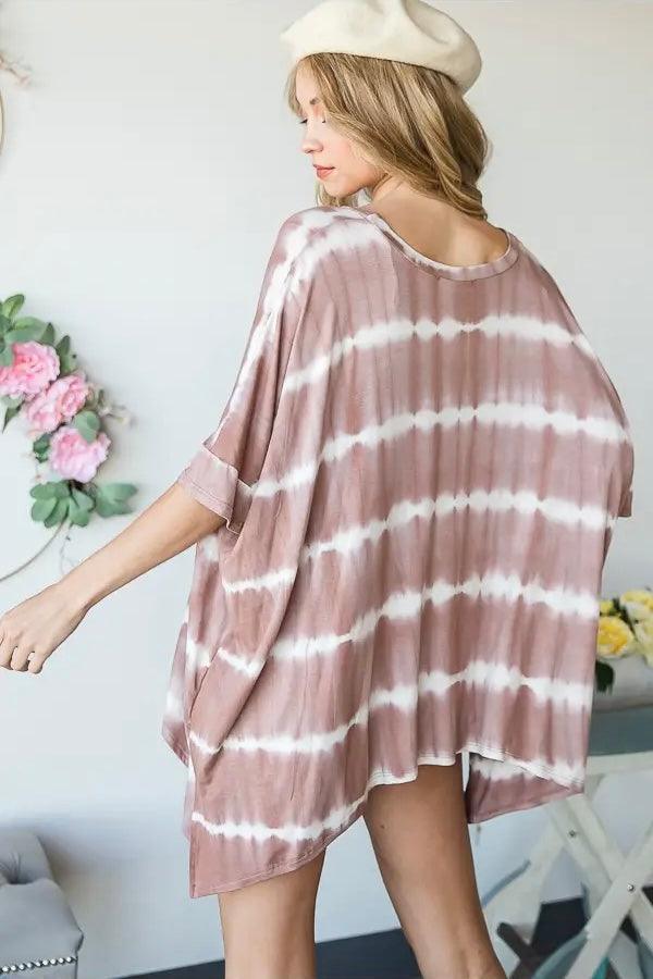Woman wearing a pink striped tie dye tunic with rolled sleeves and a cream beret in a bright room with flowers nearby