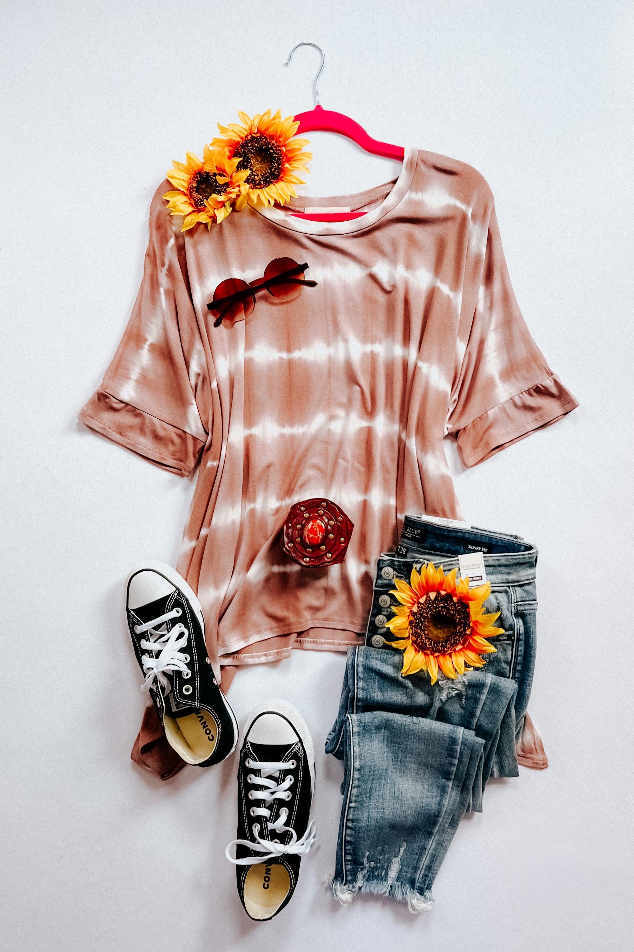 Soft brown striped tie dye top paired with distressed blue jeans, black sneakers, and sunflower accessories.