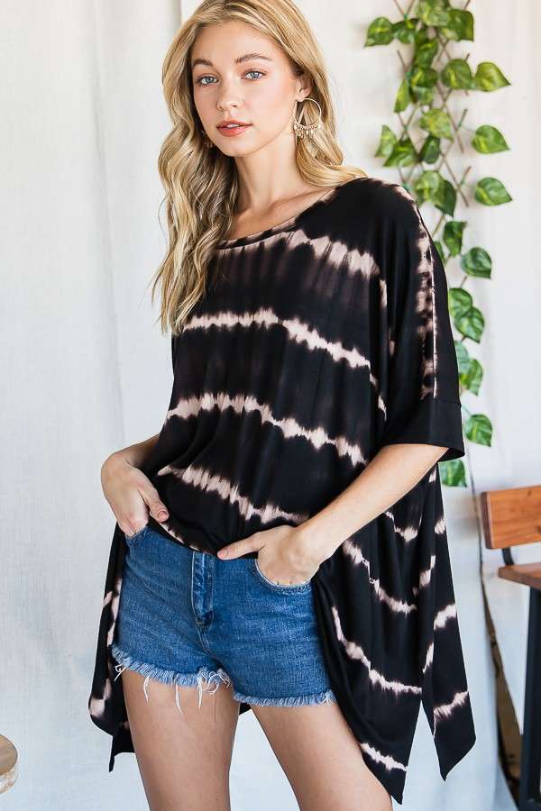 Woman wearing a loose black and beige striped tie dye top with elbow-length sleeves paired with denim shorts indoors