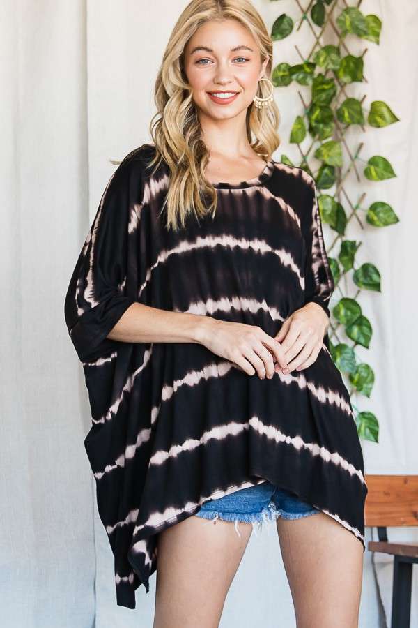 Smiling woman wearing a loose black striped tie dye tunic with rolled sleeves and denim shorts in a bright room