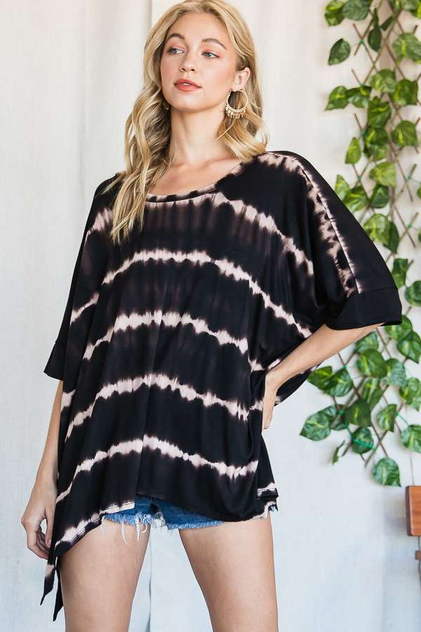 Woman wearing a loose black striped tie dye top with short sleeves and denim shorts in a casual indoor setting