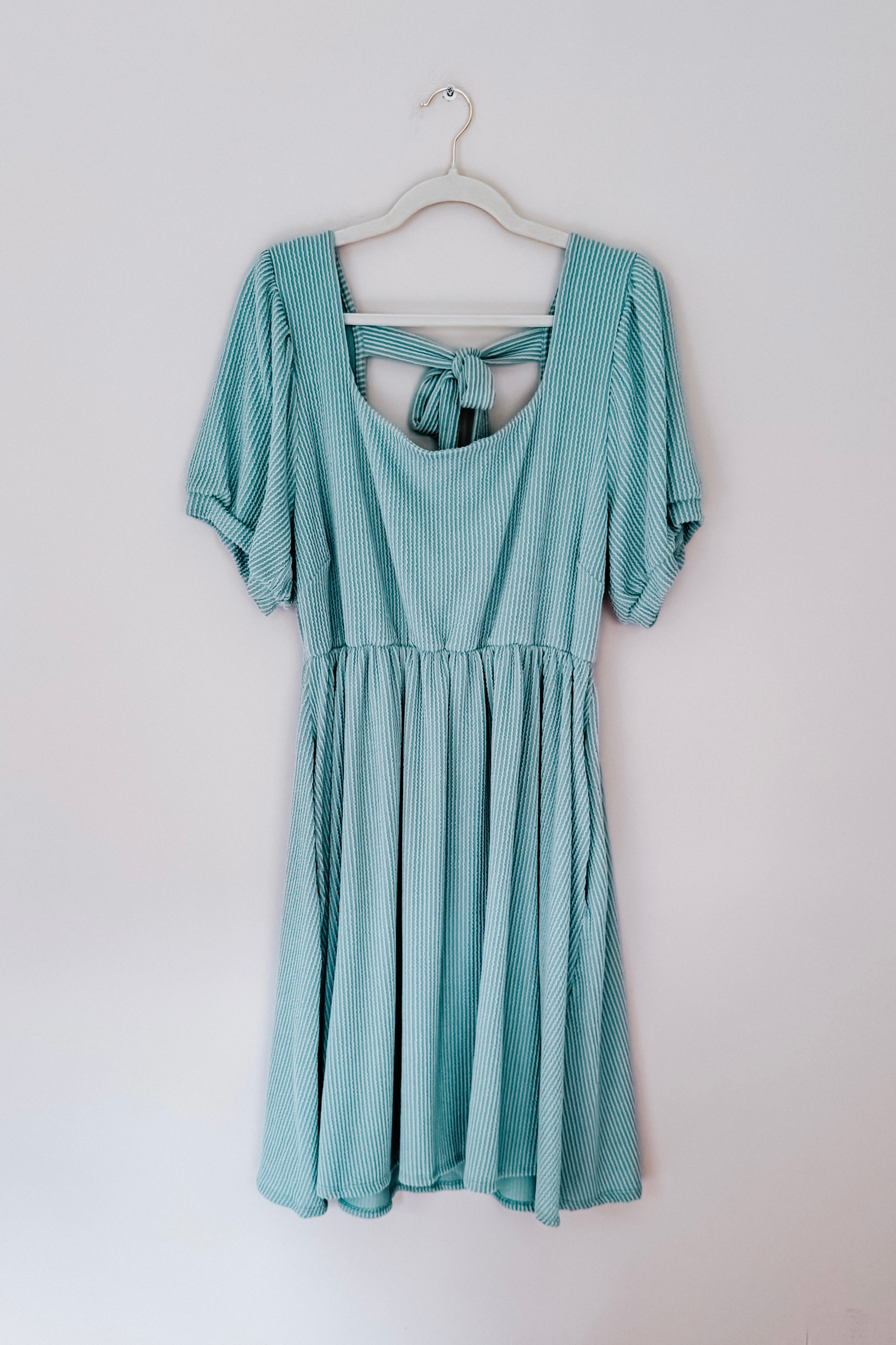 Light sage knit dress with puff sleeves and a back tie detail hanging on a white hanger against a plain wall