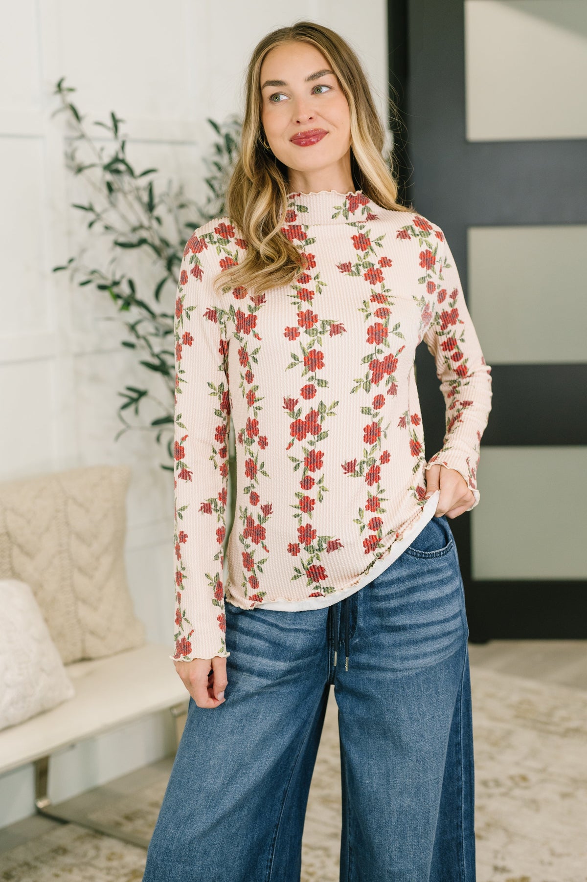 Woman wearing a beige high neck floral ribbed top with wide leg jeans in a bright modern home interior