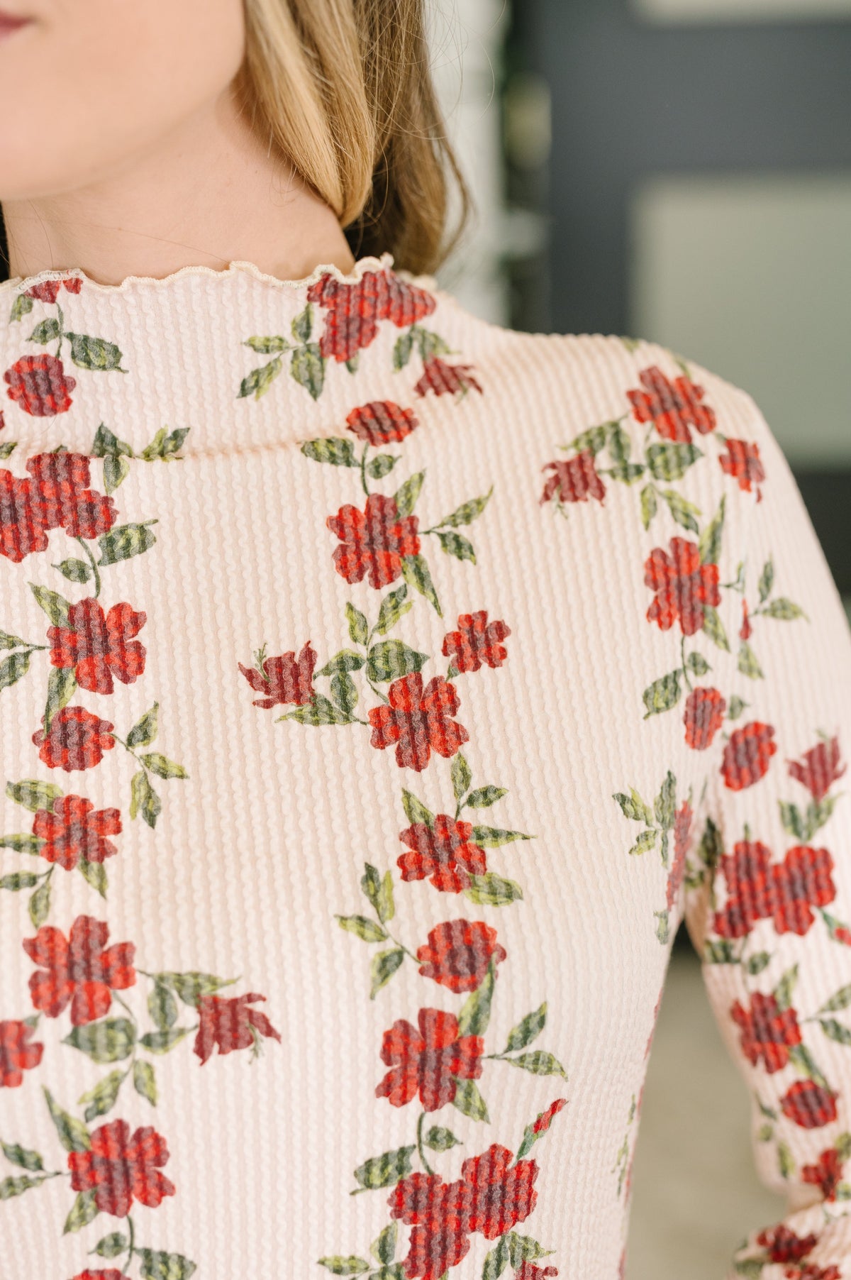 Close-up of a woman wearing a beige floral high neck top with cable ribbed knit texture and long sleeves
