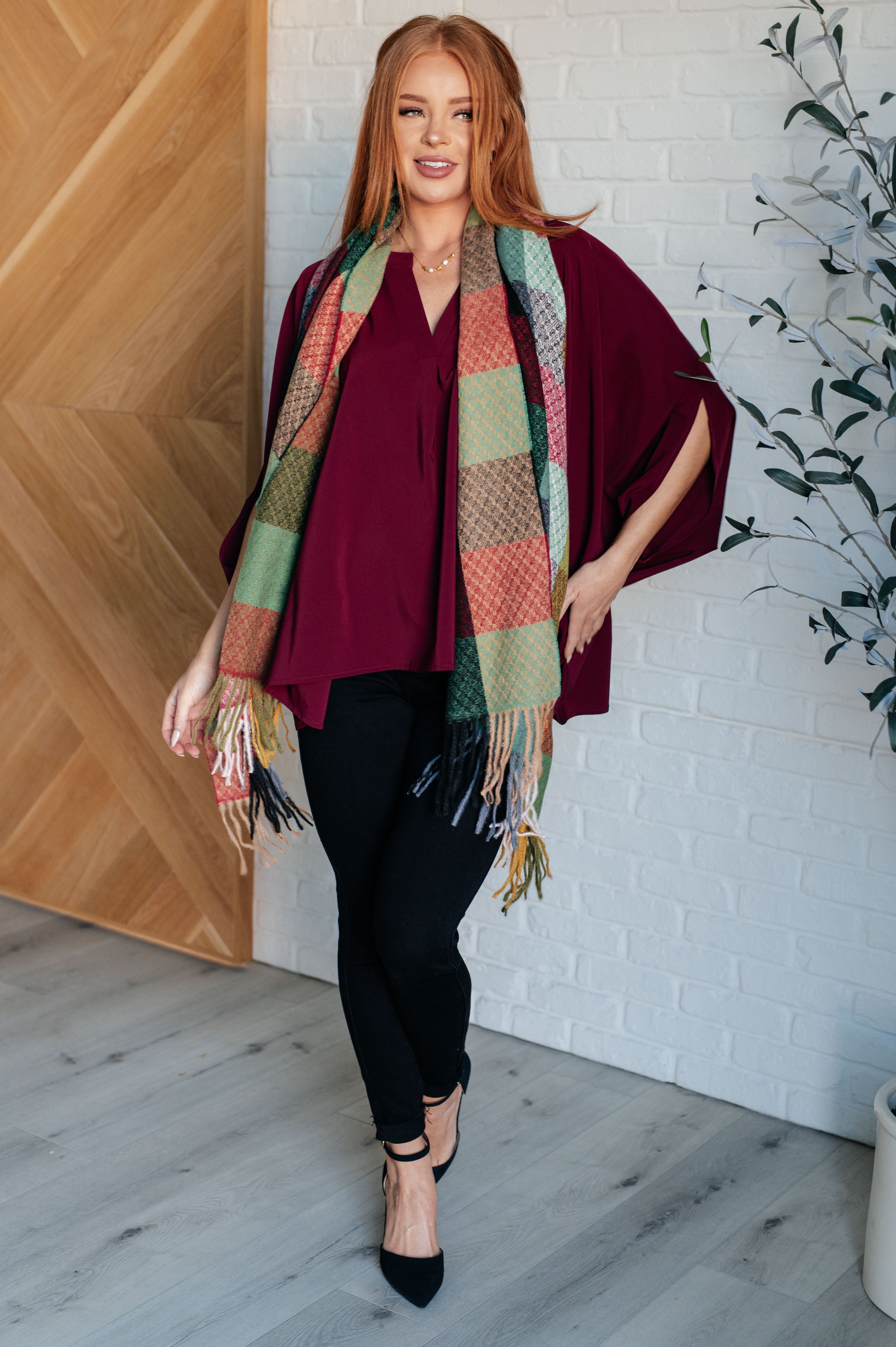 Woman wearing a wine-colored blouse with flowy sleeves and patterned scarf, paired with black pants and heels indoors