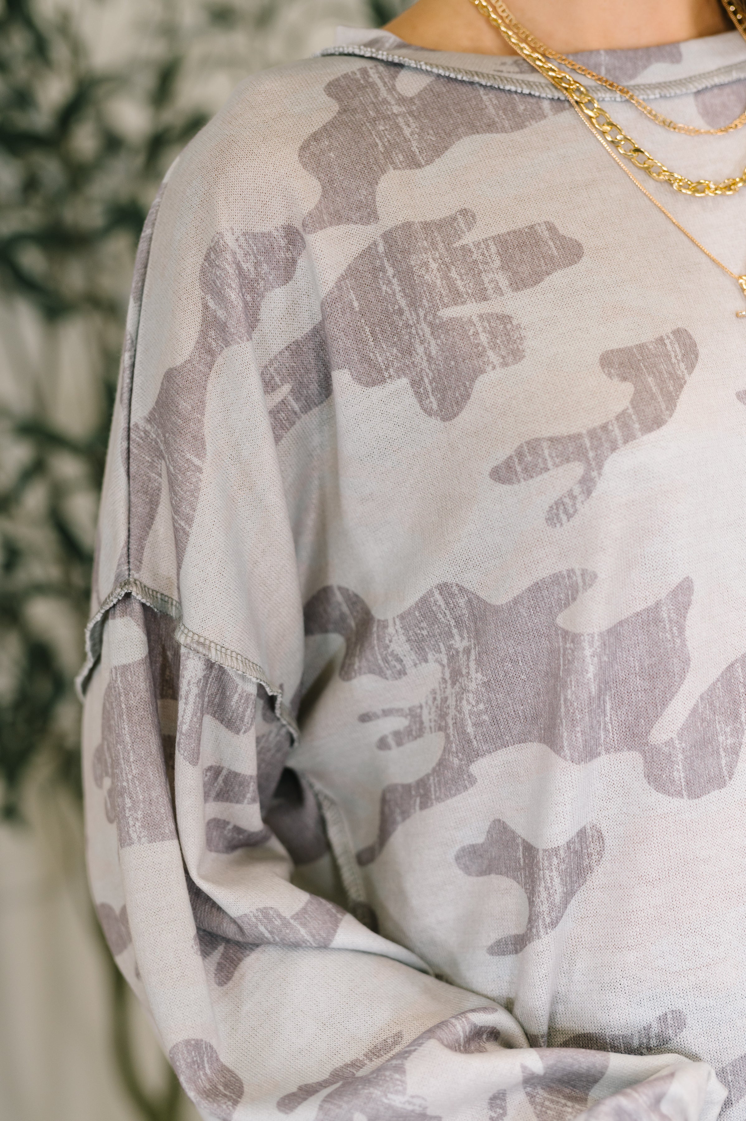 Close-up of grey camo print drop shoulder top paired with layered gold chain necklaces on model