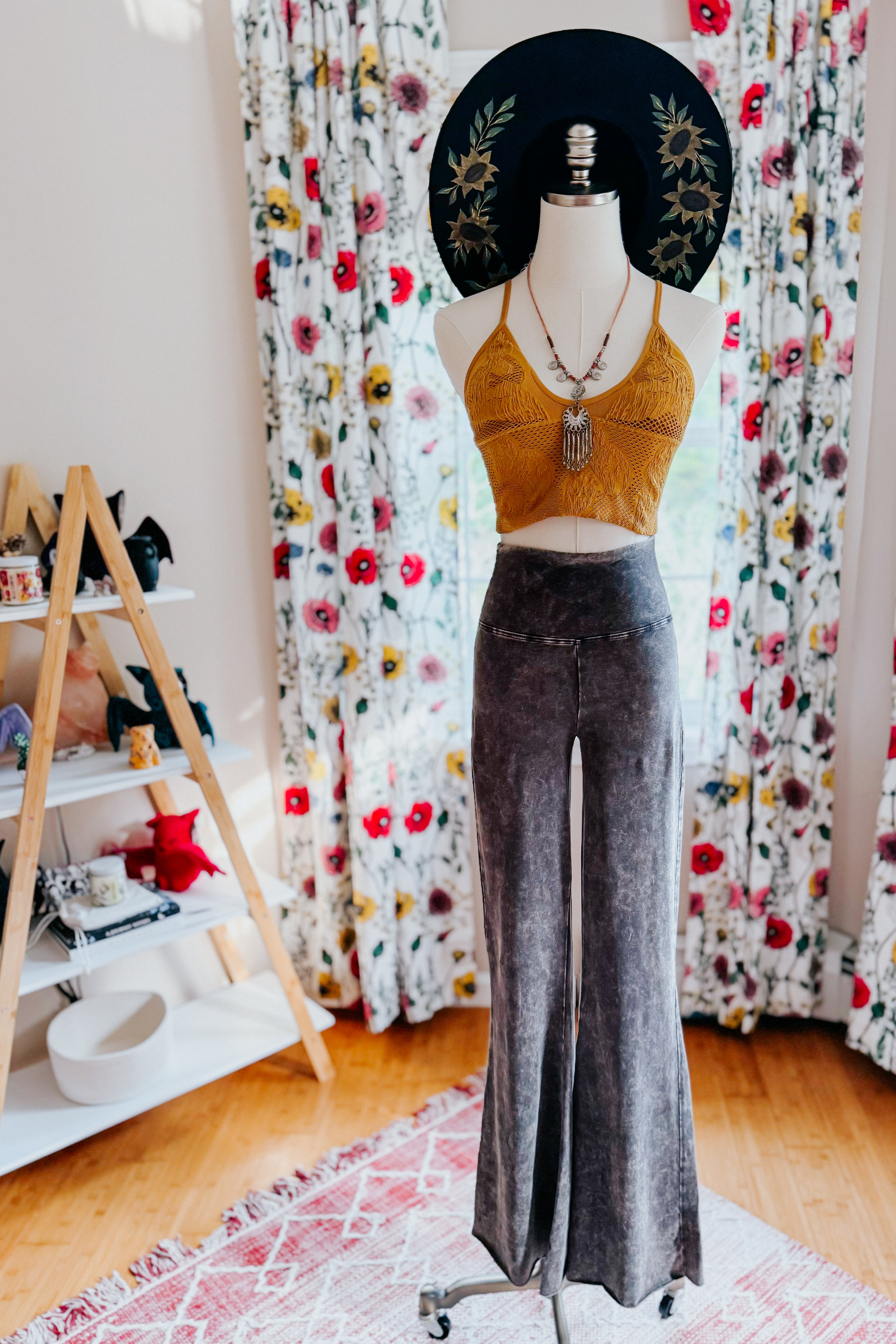 Mannequin dressed in mustard crochet crop top with layered necklaces and acid wash ash black flared pants indoors