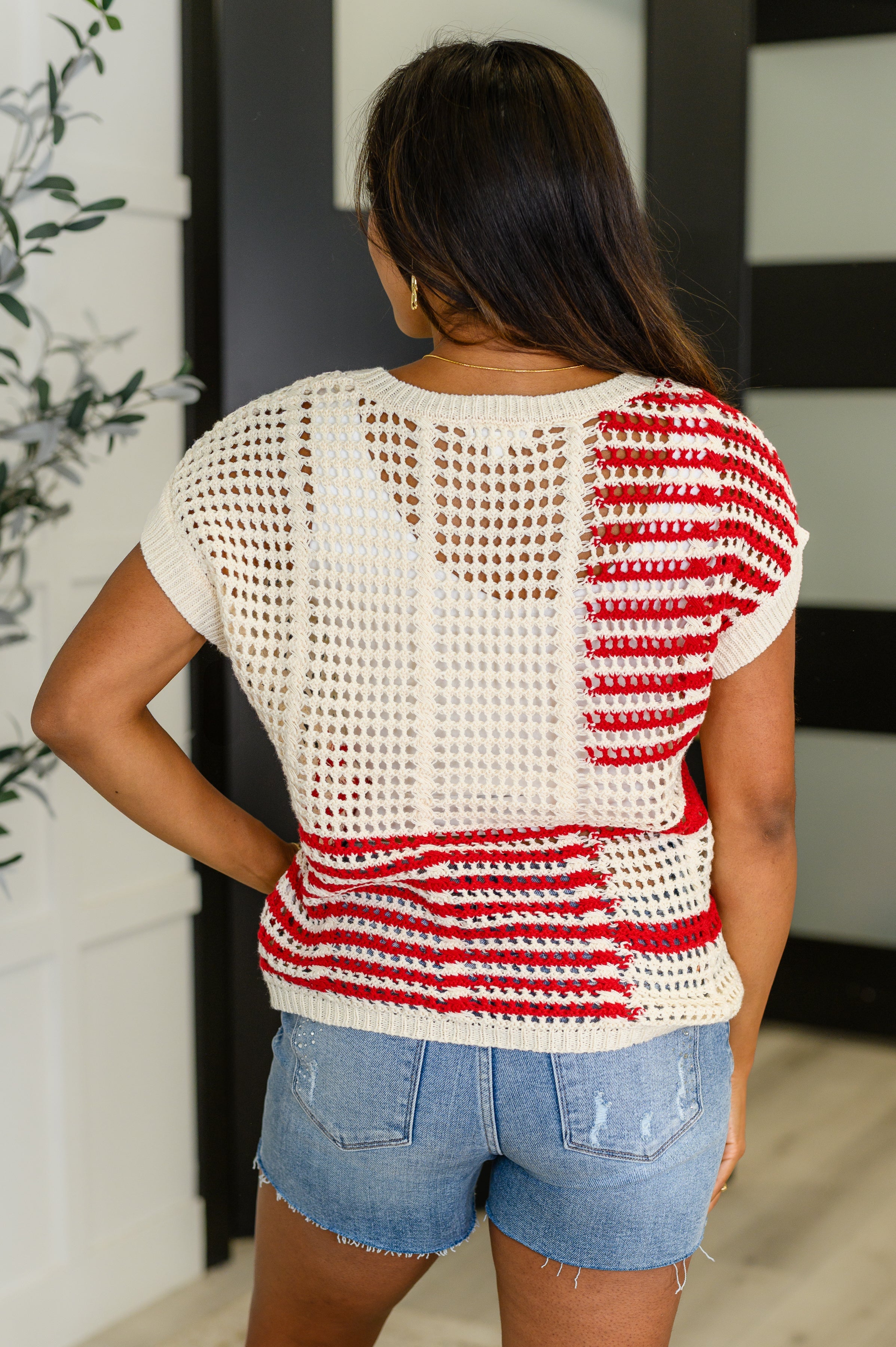 Woman wearing red striped open-knit top with cream accents paired with denim shorts indoors by black and white door