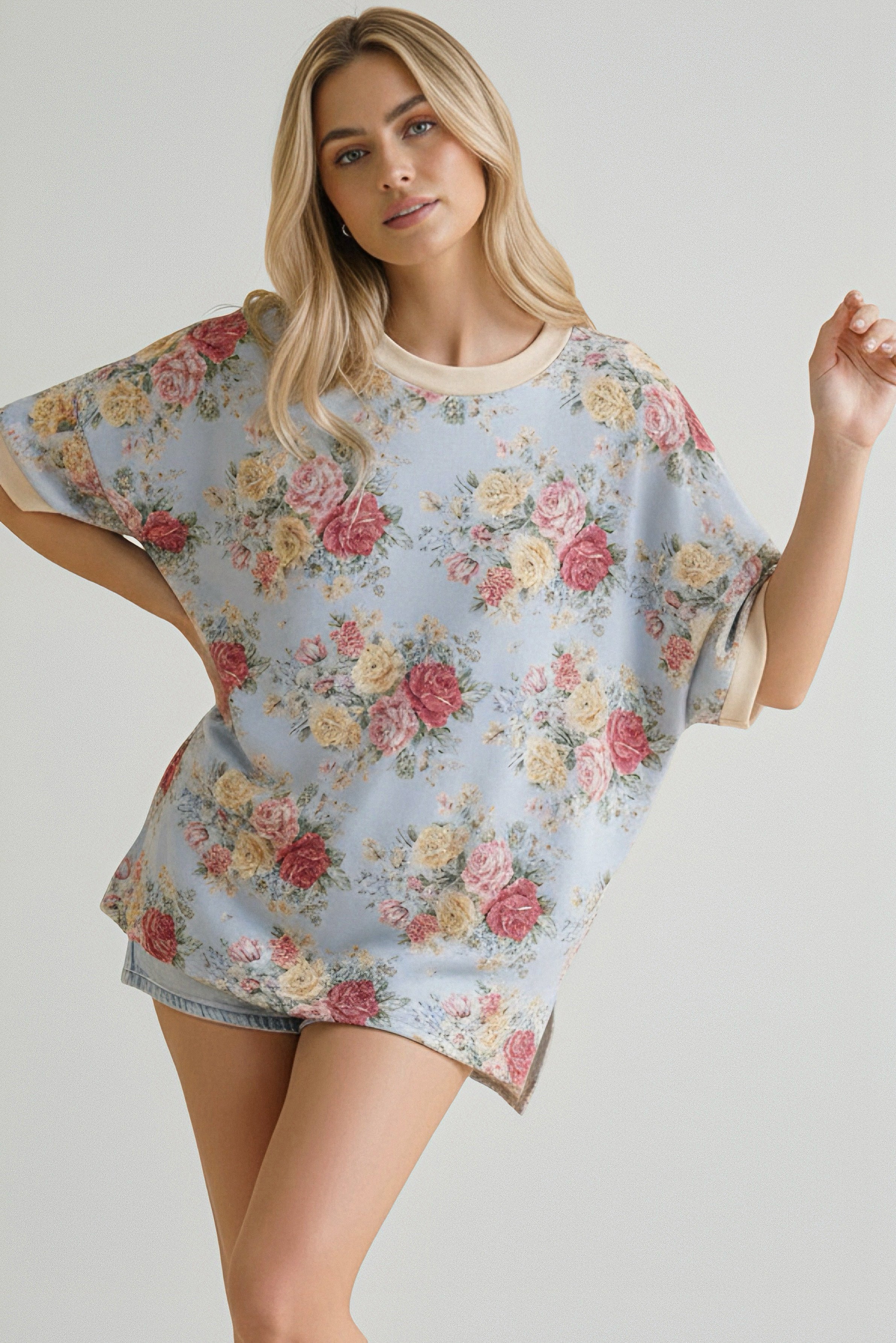 Woman wearing a loose blue top with pink and yellow floral pattern and beige trim paired with light denim shorts