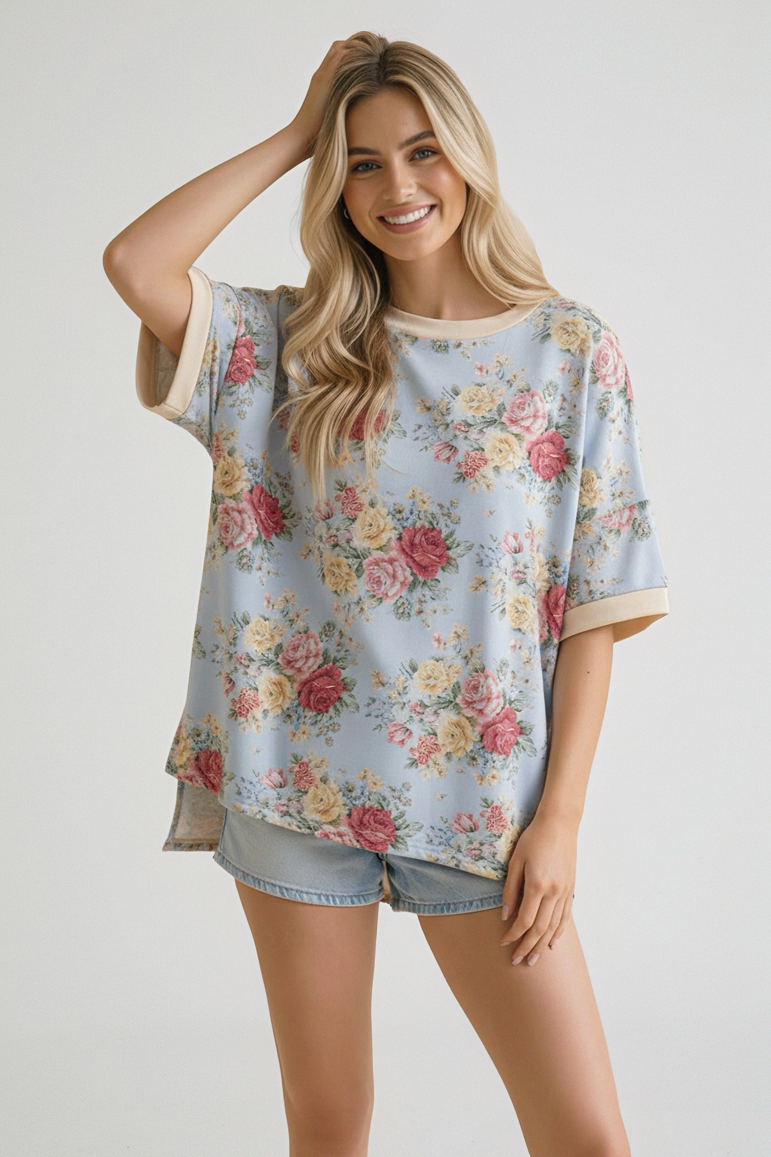 Smiling woman wearing a loose blue top with multicolored floral print and beige trim paired with light denim shorts