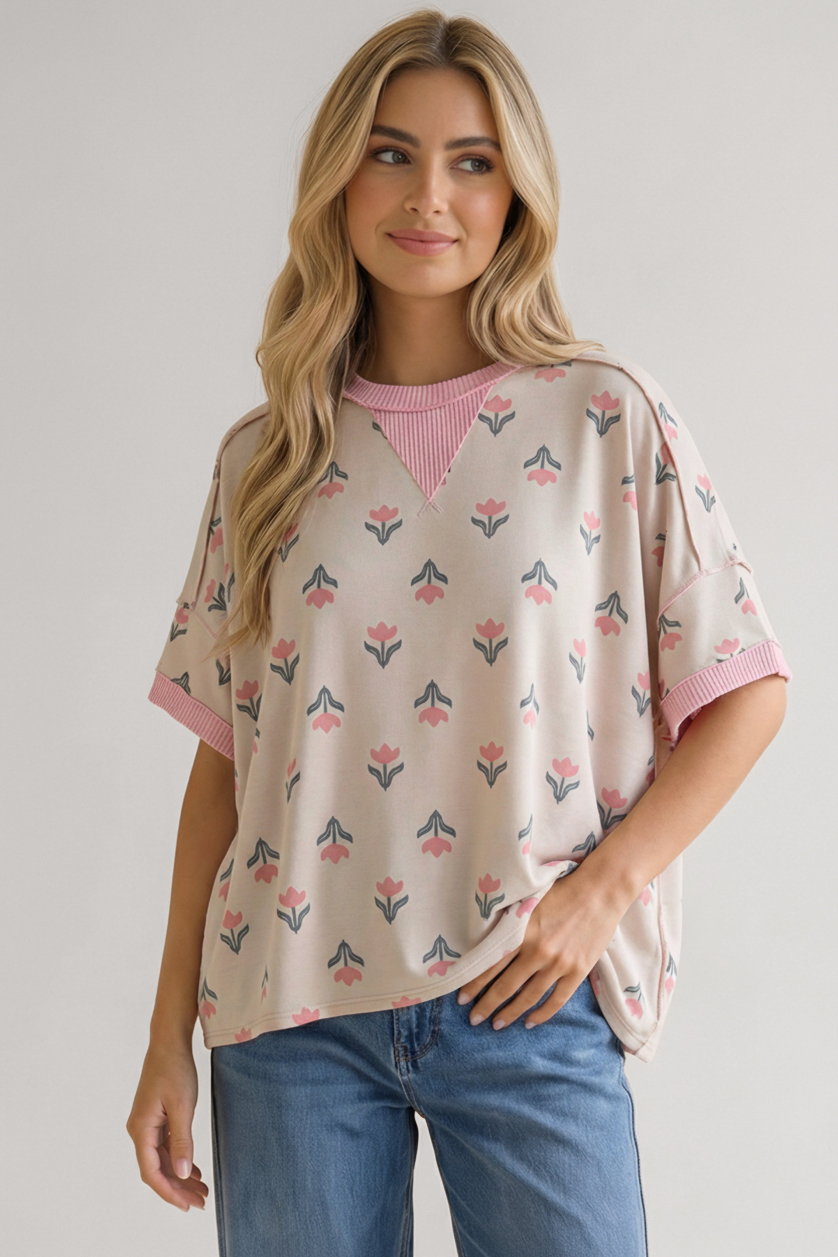 Woman wearing relaxed pink floral tee with ribbed crew neck and cuffs paired with blue jeans against neutral backdrop