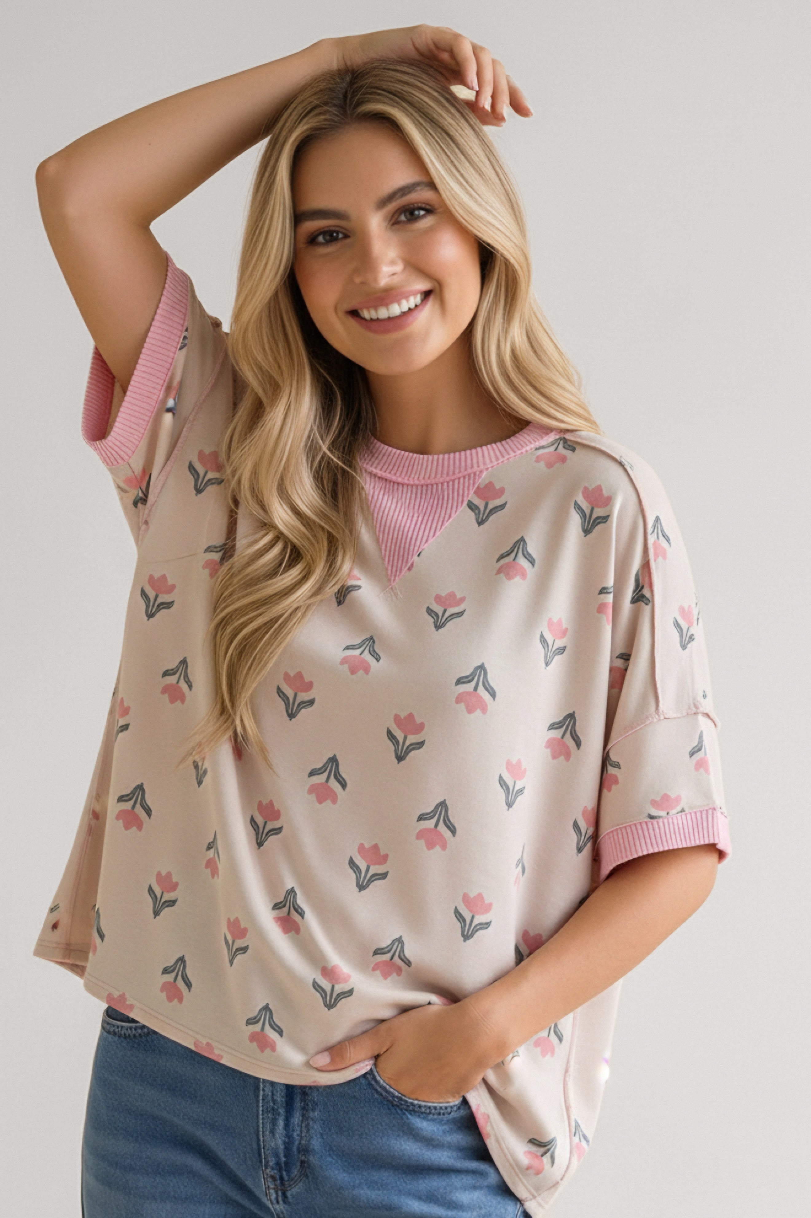 Smiling woman wearing a relaxed pink floral tee with ribbed neckline and cuffs paired with blue jeans indoors