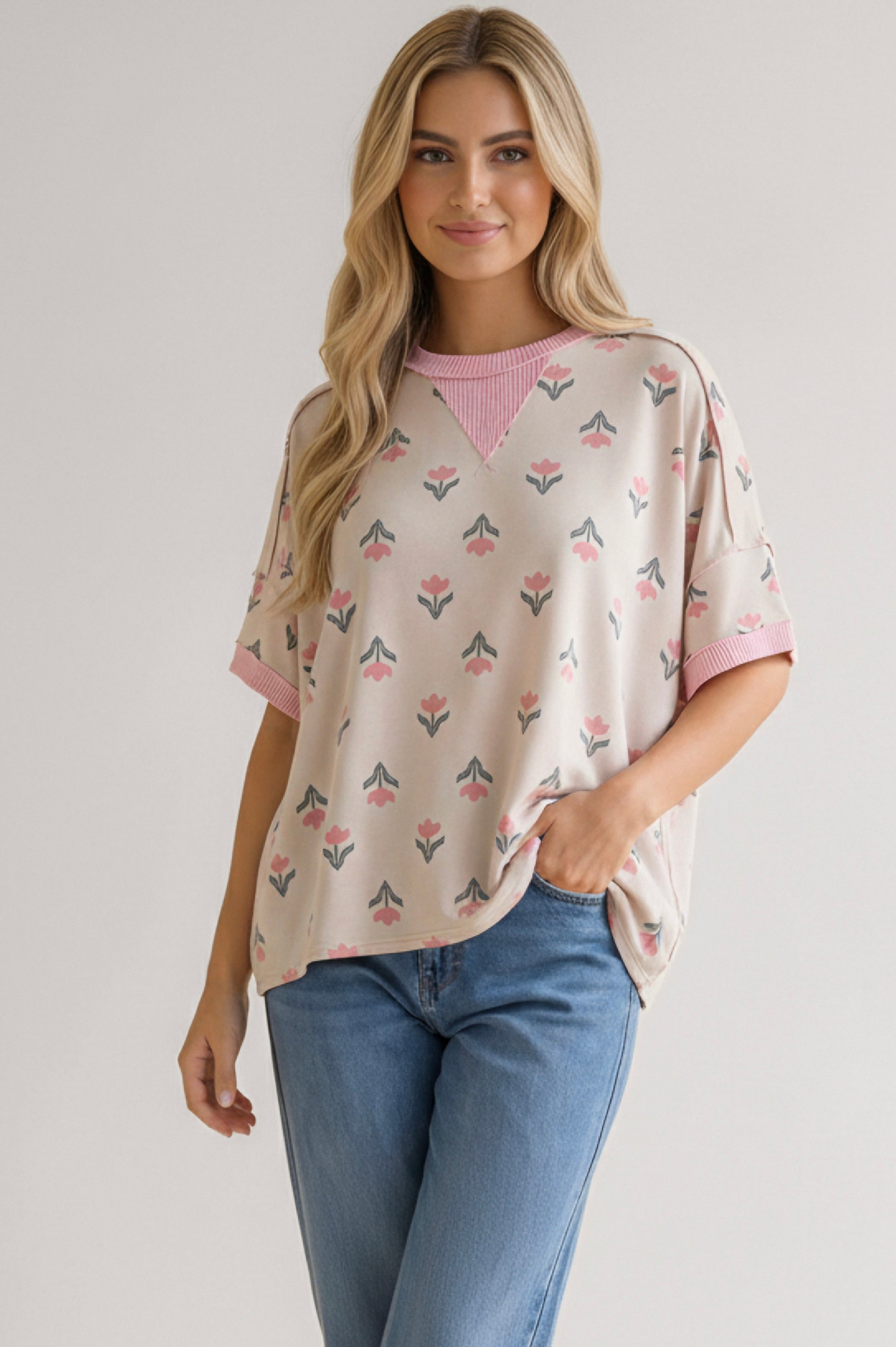 Woman wearing relaxed pink floral tee with ribbed neckline and cuff details paired with blue jeans against neutral backdrop